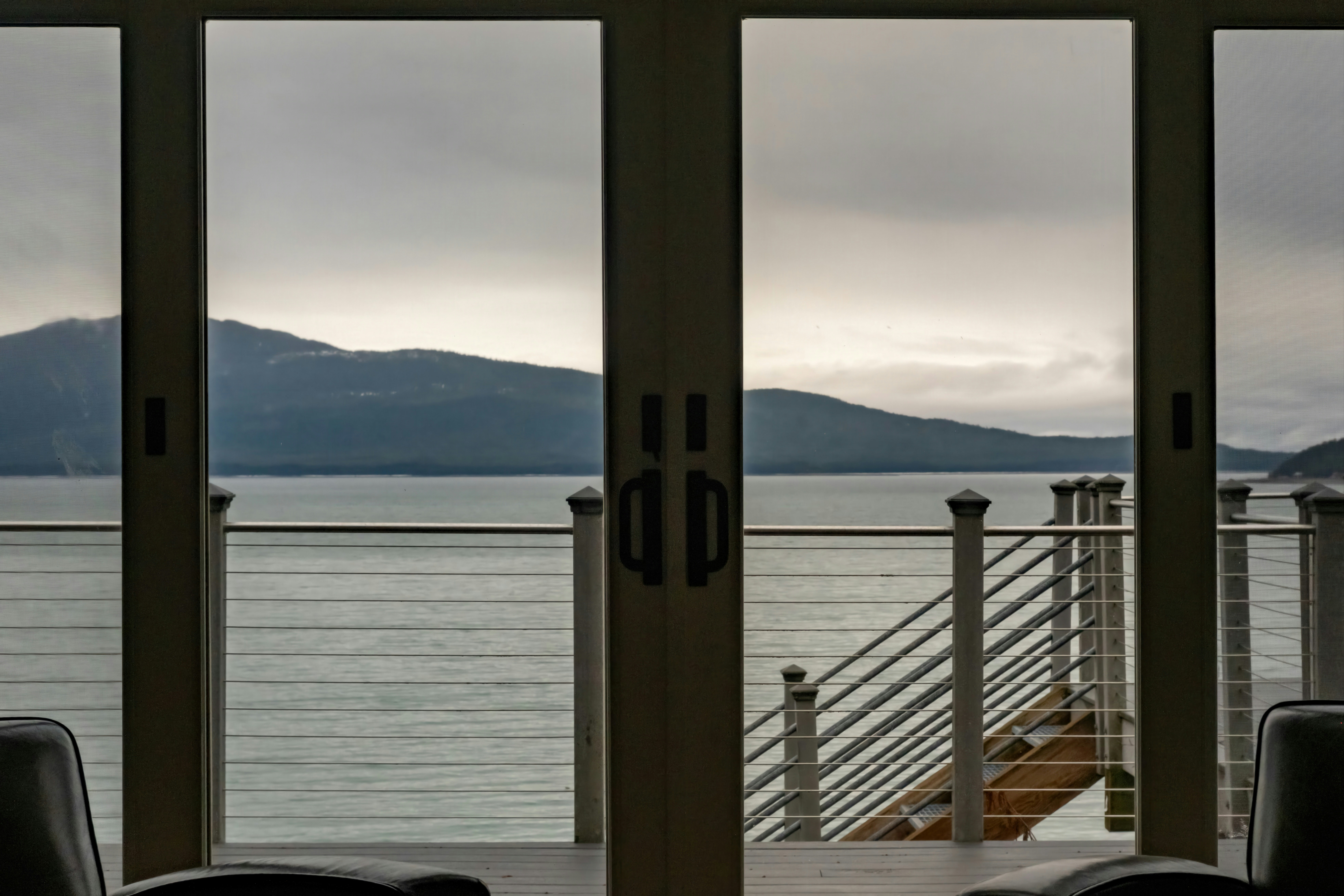 View of a calm sea and mountains through glass doors.