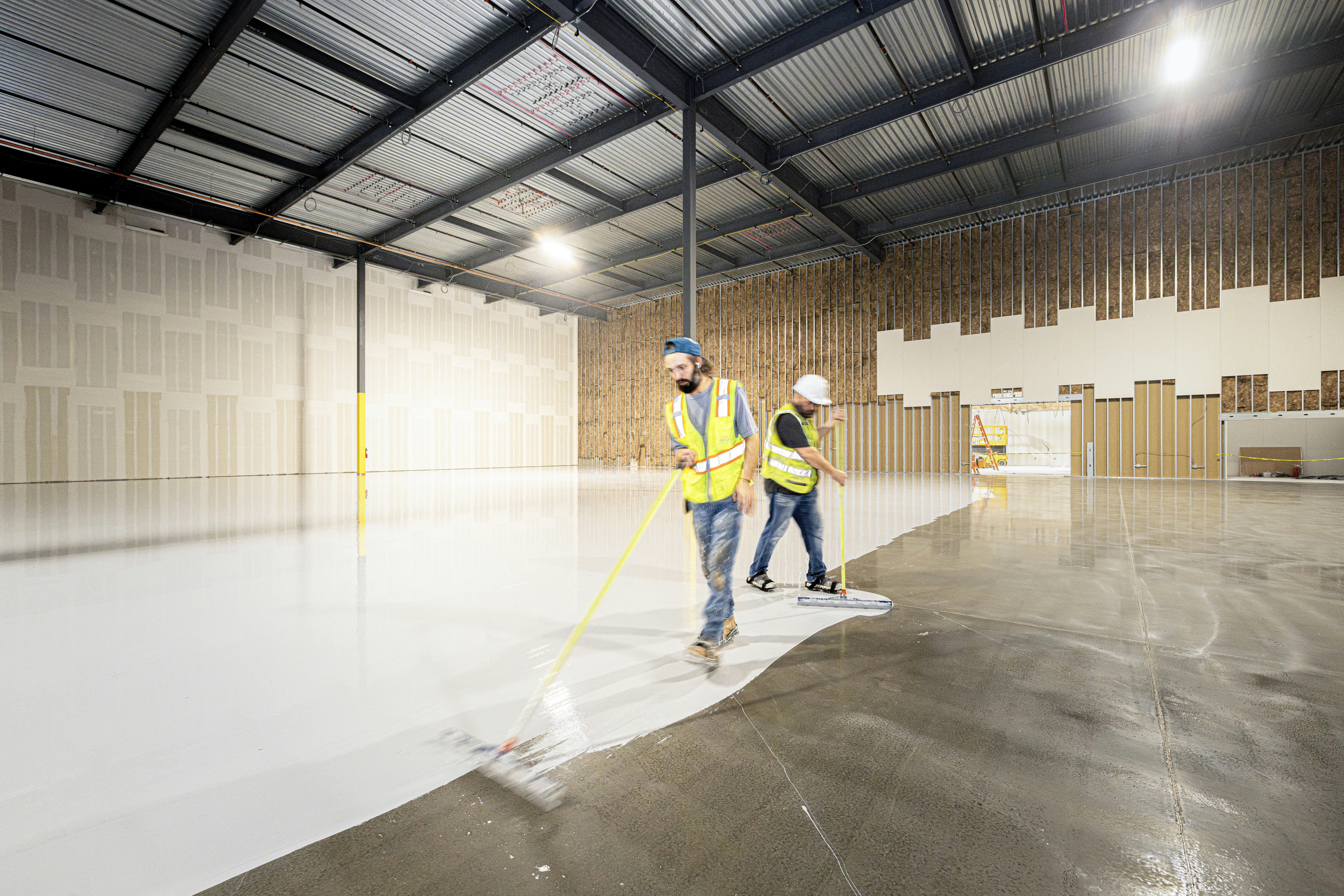 Workers painting the floor of a large empty warehouse.