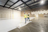 Workers painting the floor of a large empty warehouse.