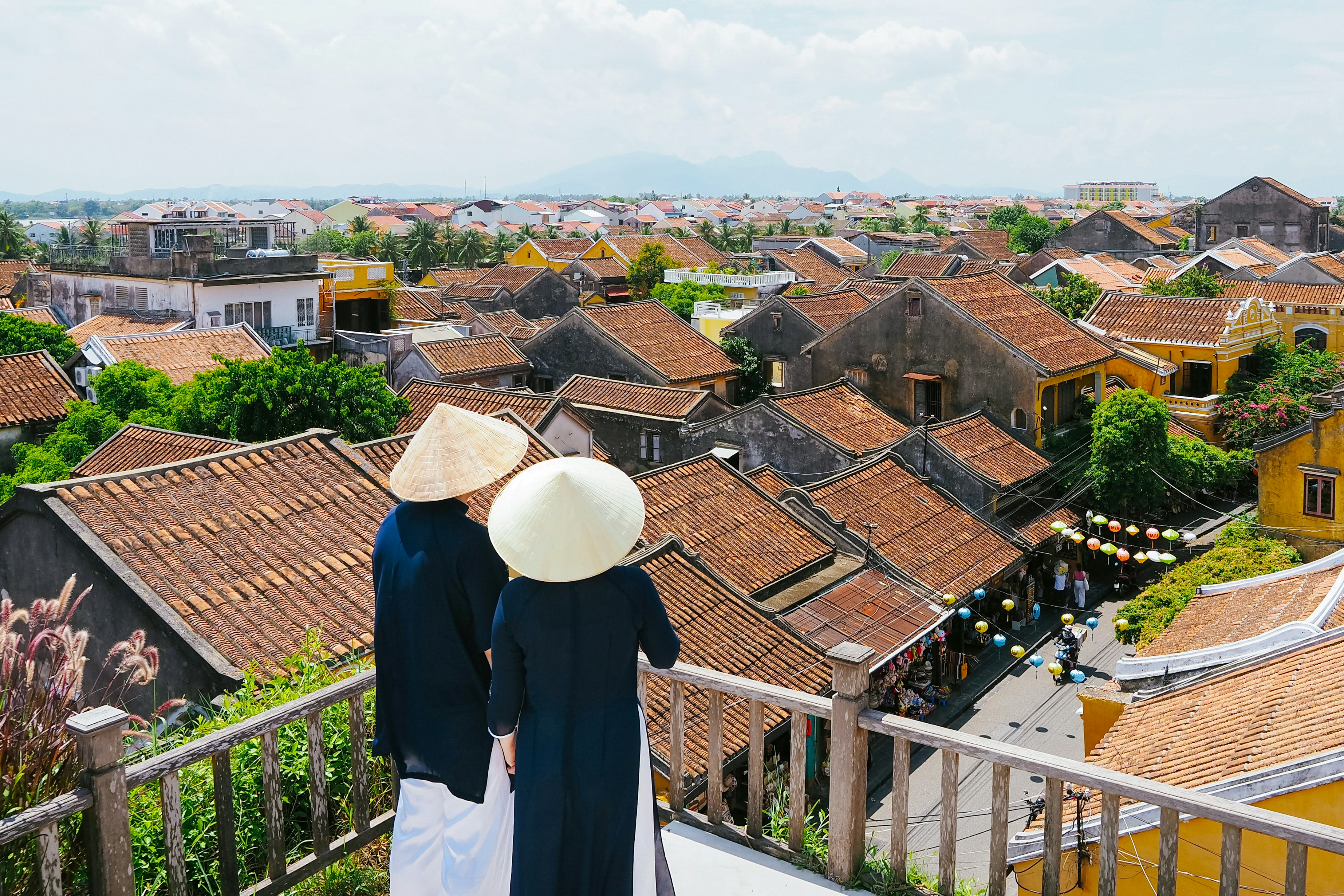 Two people in conical hats overlook a historic town.