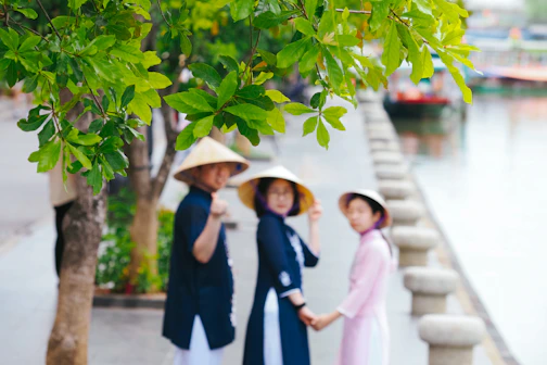 Three people in conical hats by a canal