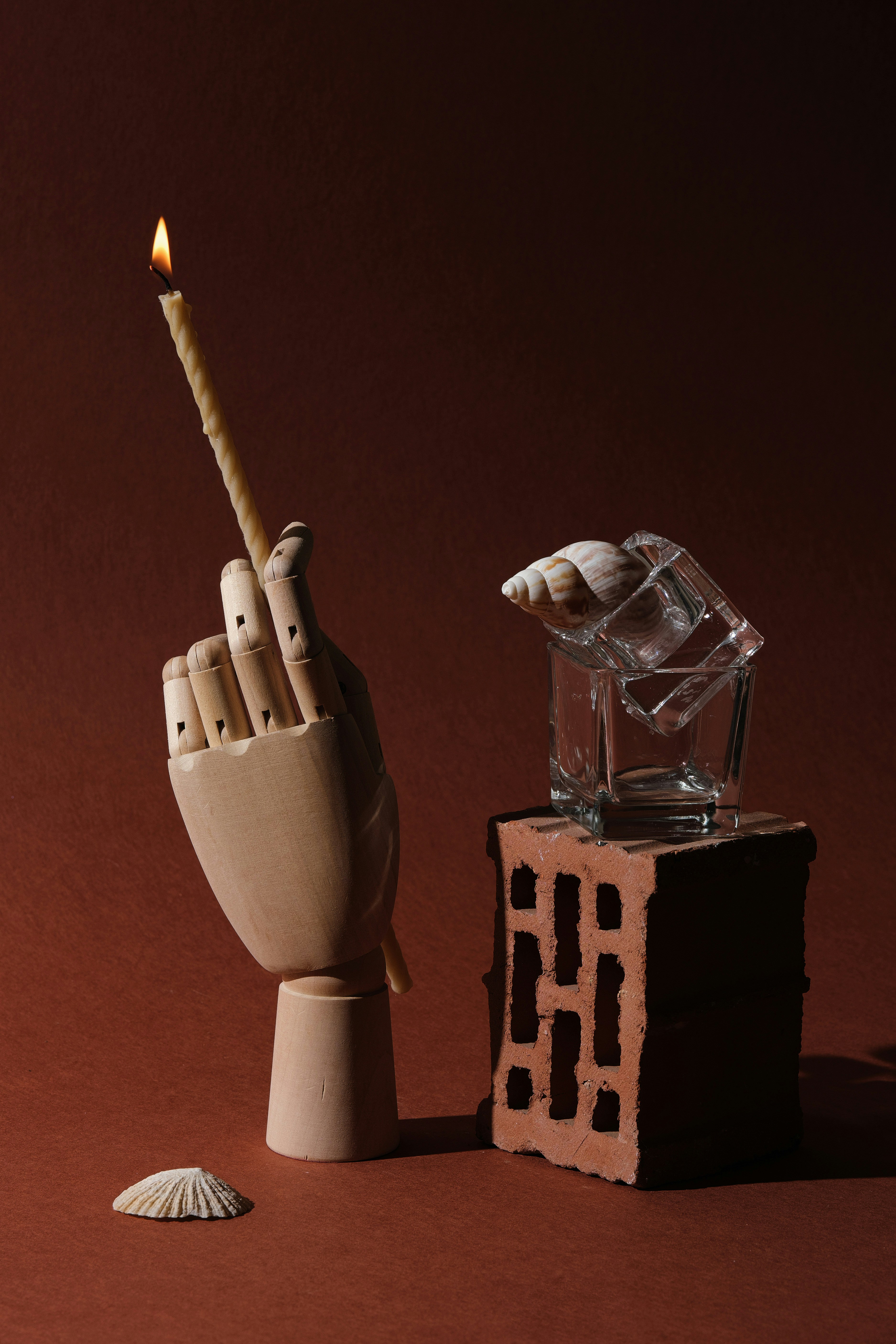 Eine hölzerne Hand hält eine brennende Kerze neben Ziegeln und Glas.