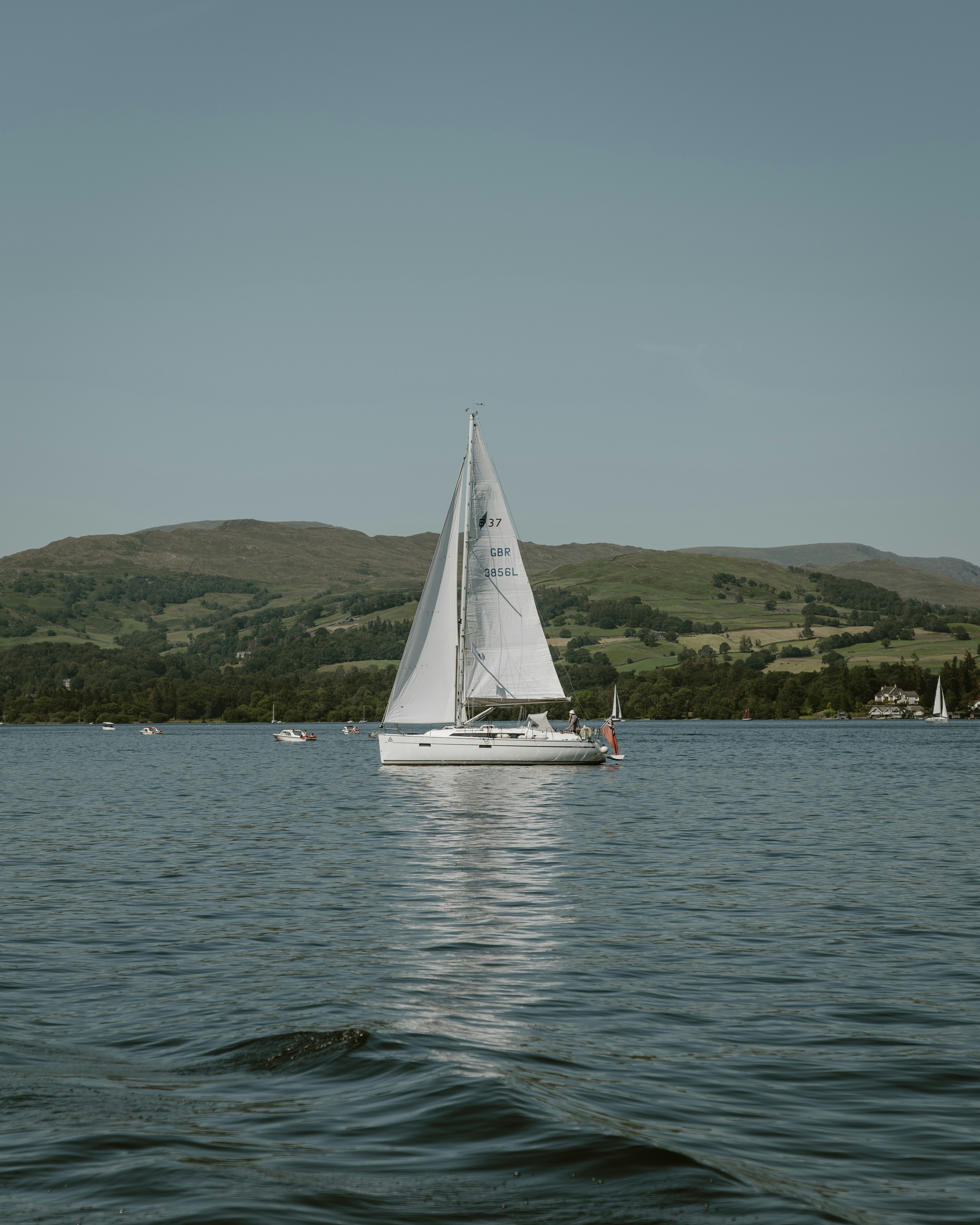 A white sailboat glides across a calm blue lake.