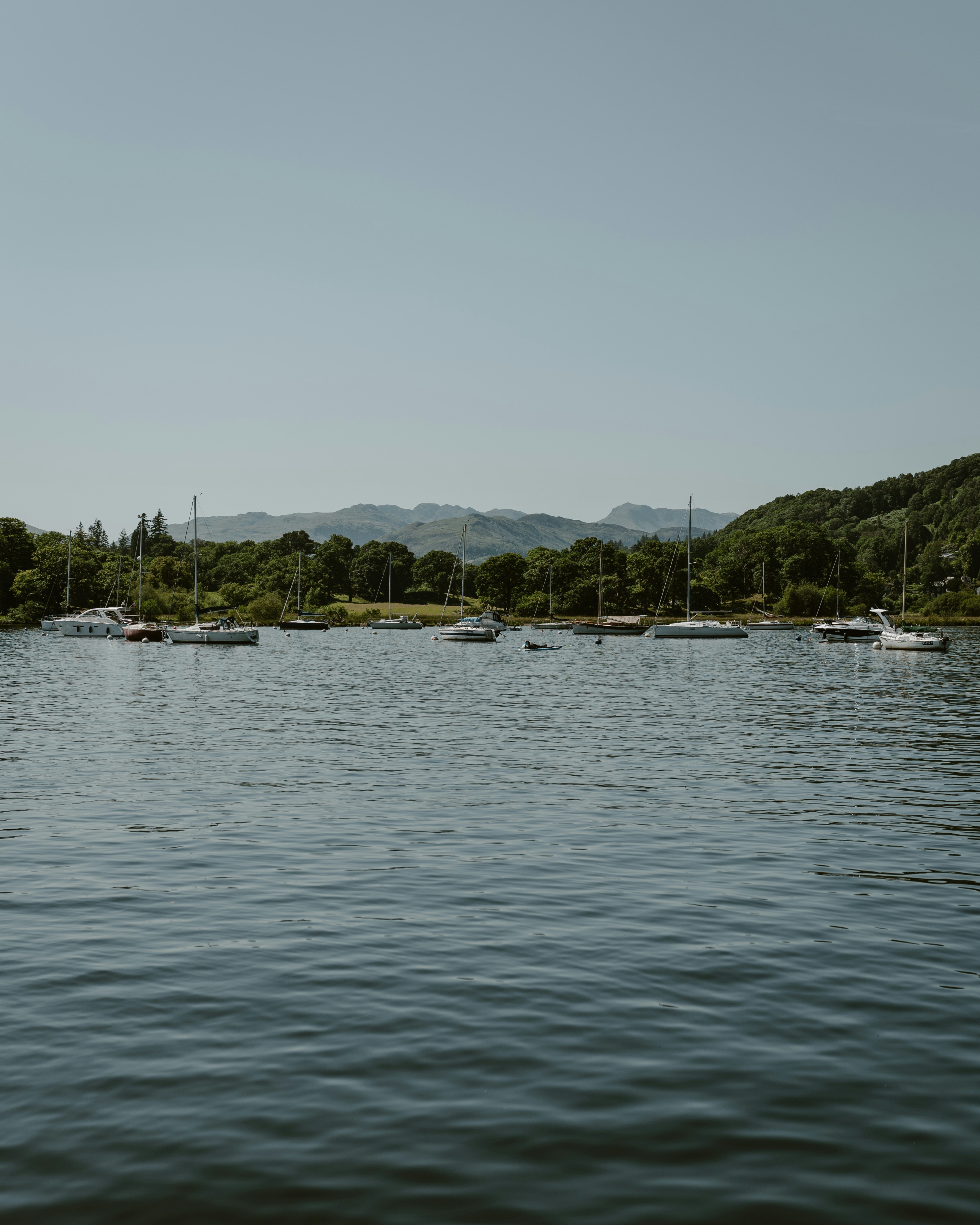 Sailboats anchored on a calm lake with green hills.