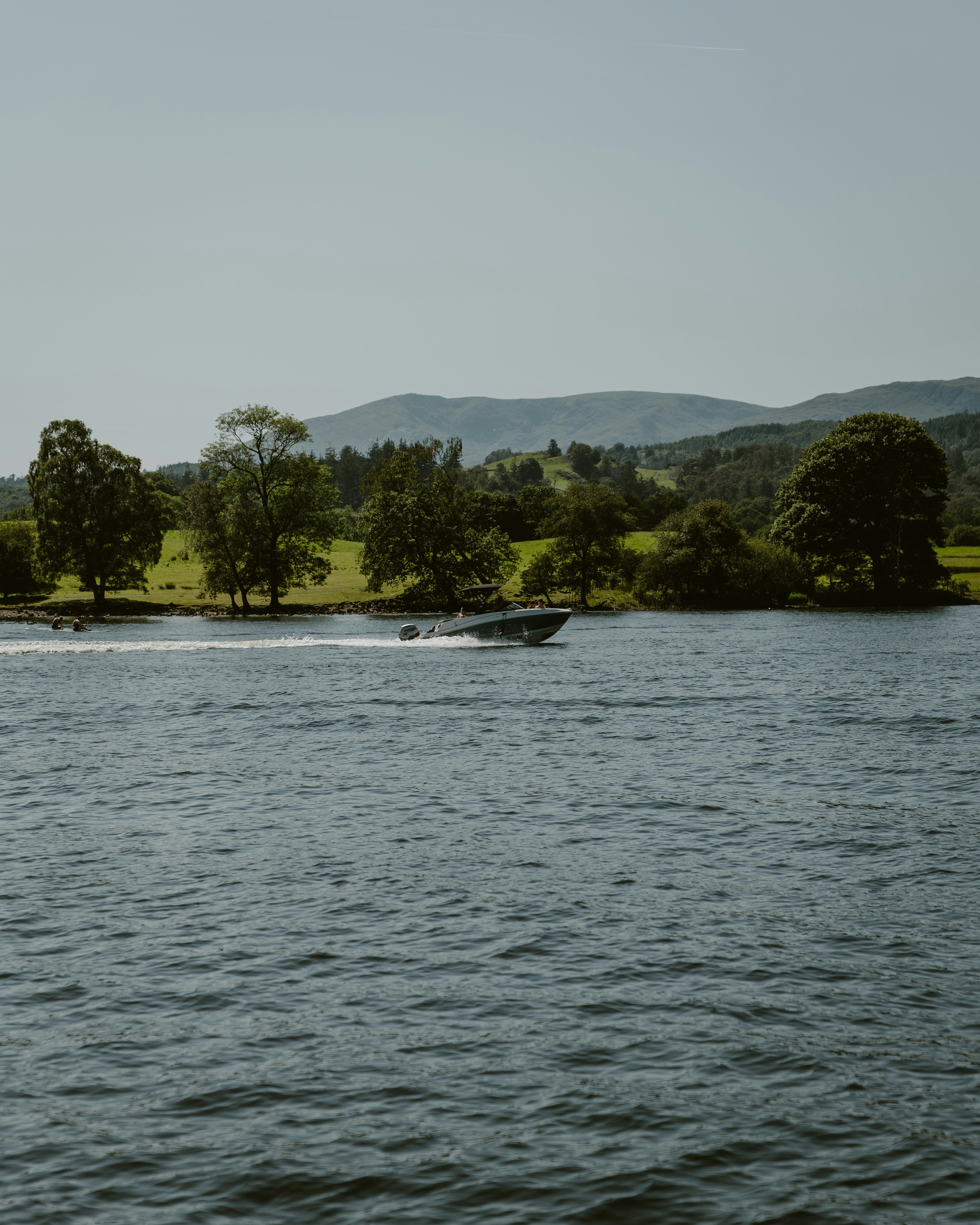 Motorboat speeding across a calm lake with green hills.