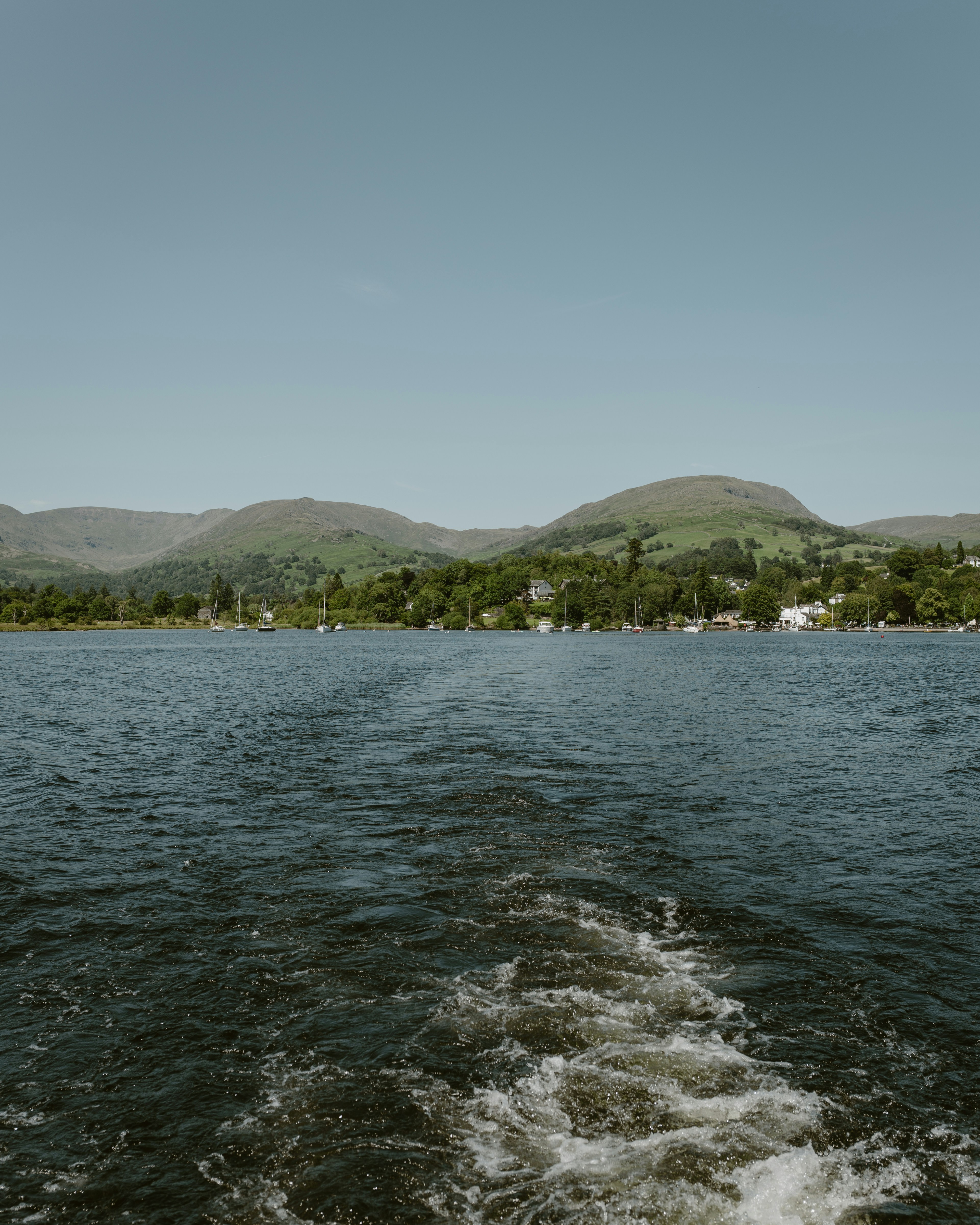 Wake trails on a lake with green hills beyond.