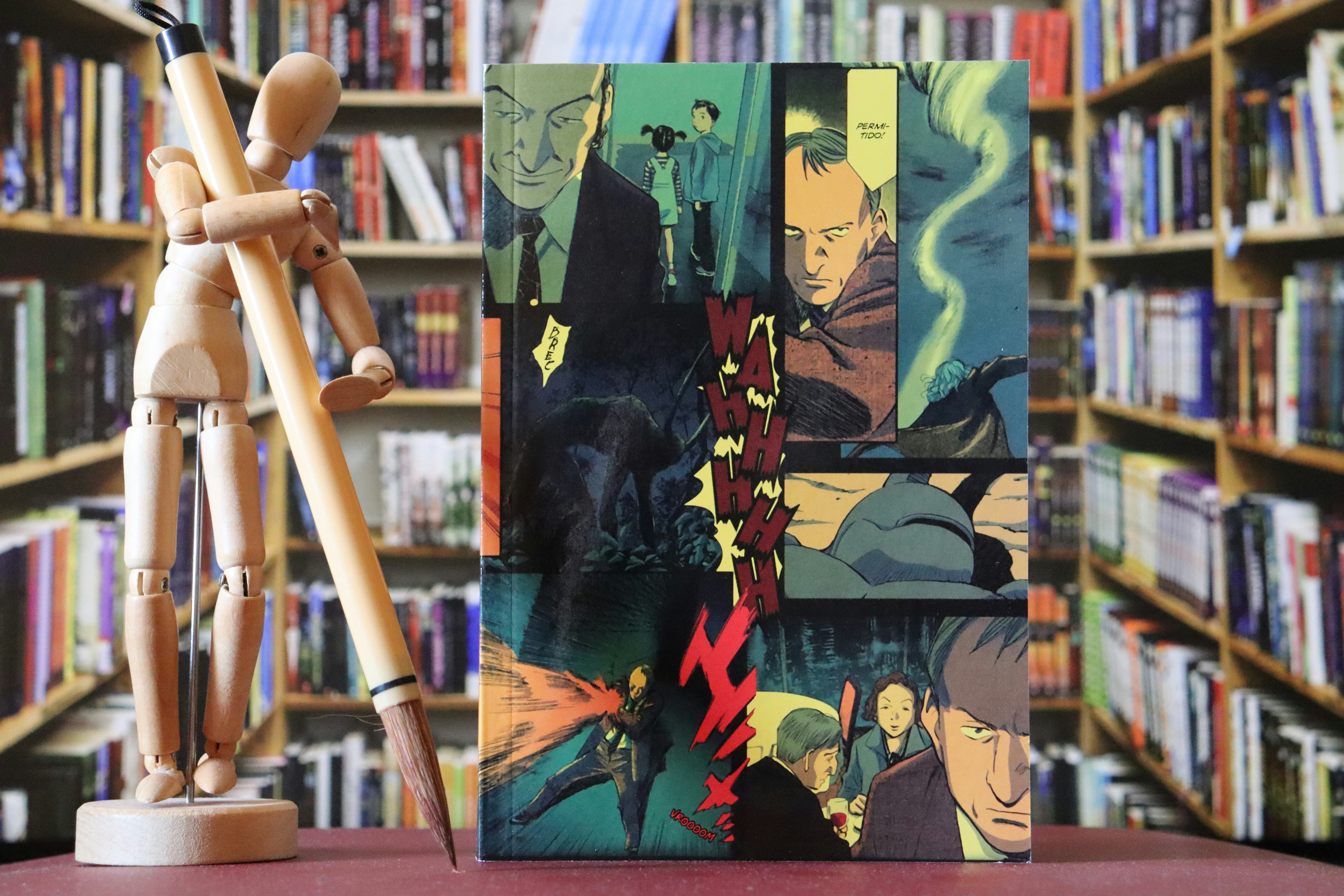 Manequim de madeira e livro de anime em frente às estantes