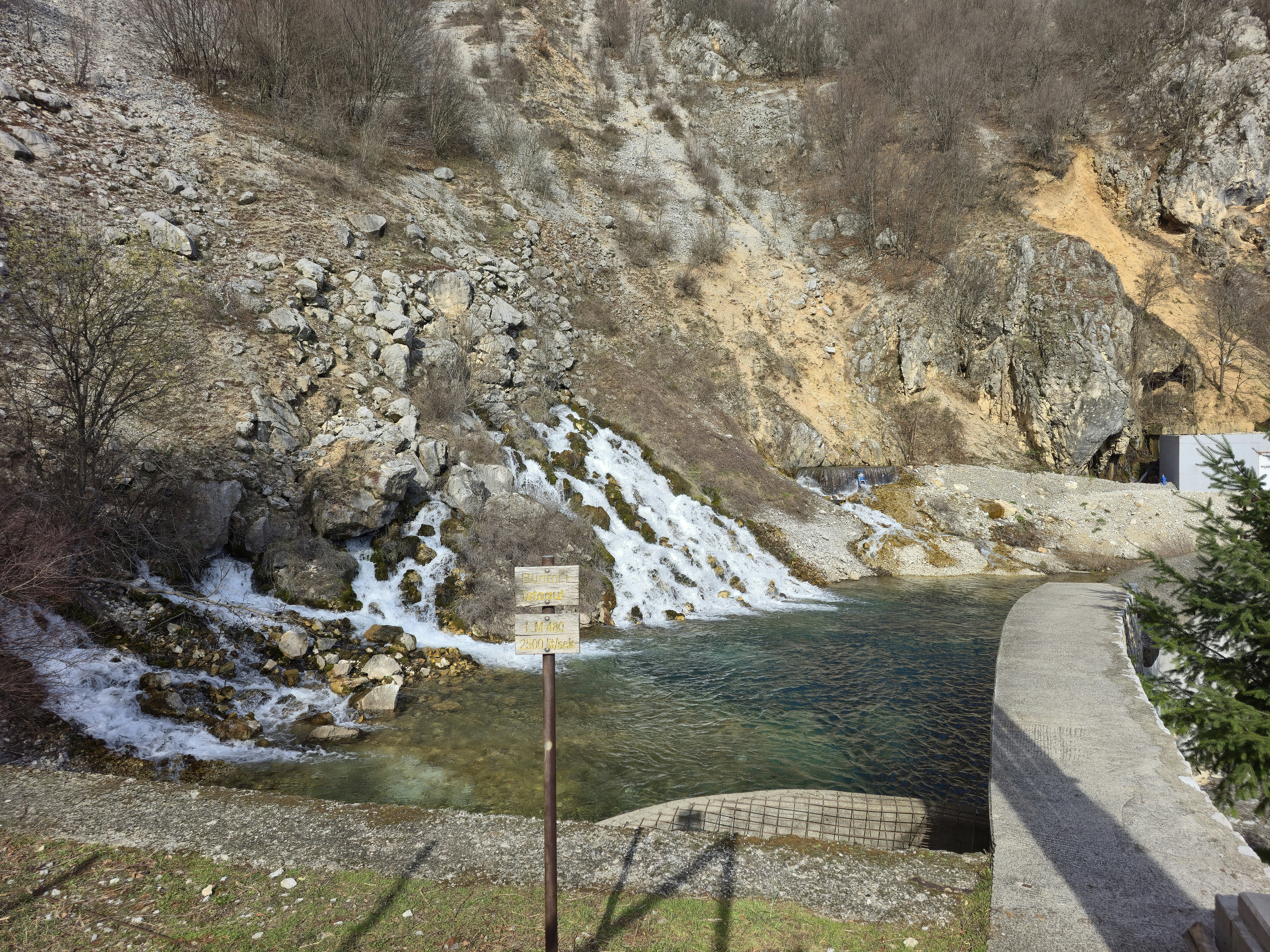 Waterfall cascading into a clear pool near rocky hills.