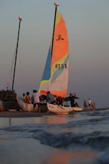 Sailboat with colorful sails on a beach at sunset.