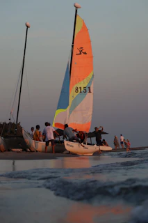 Sailboat with colorful sails on a beach at sunset.
