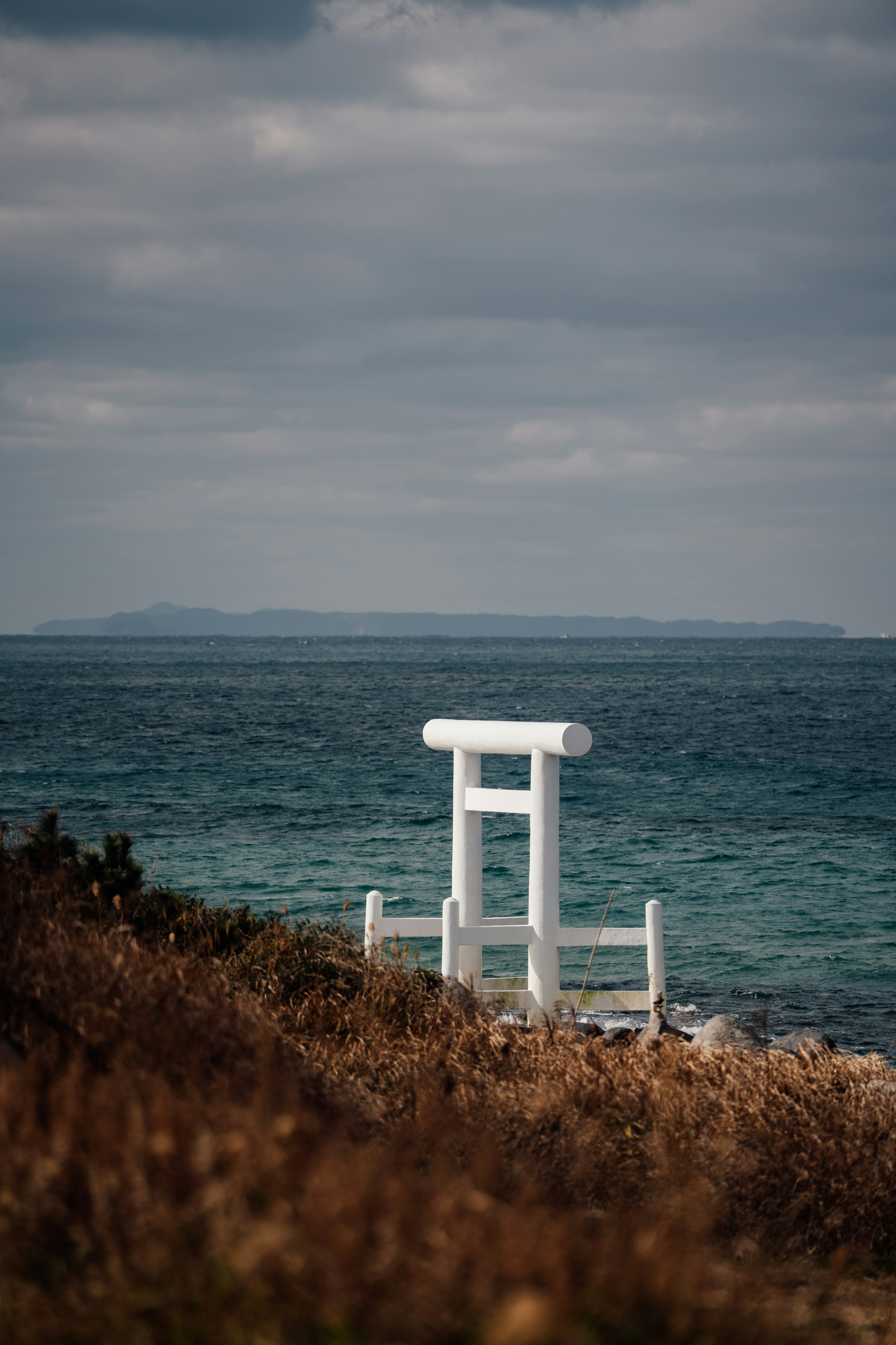 Weißes Torii-Tor an einem grasbewachsenen Ufer am Meer.