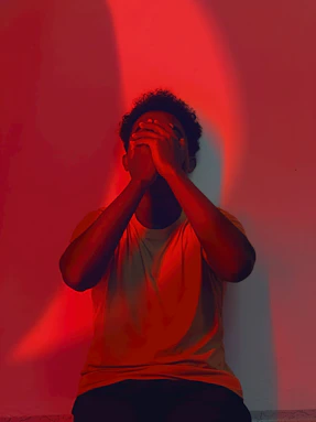Person covering face with hands under red light.