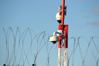 Security cameras on a tower behind barbed wire.