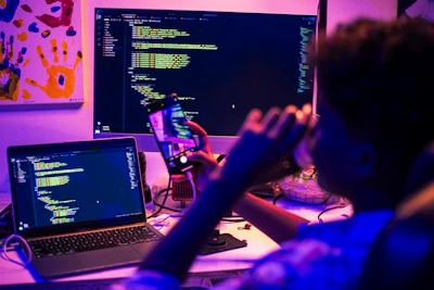 Person coding on multiple screens at night.