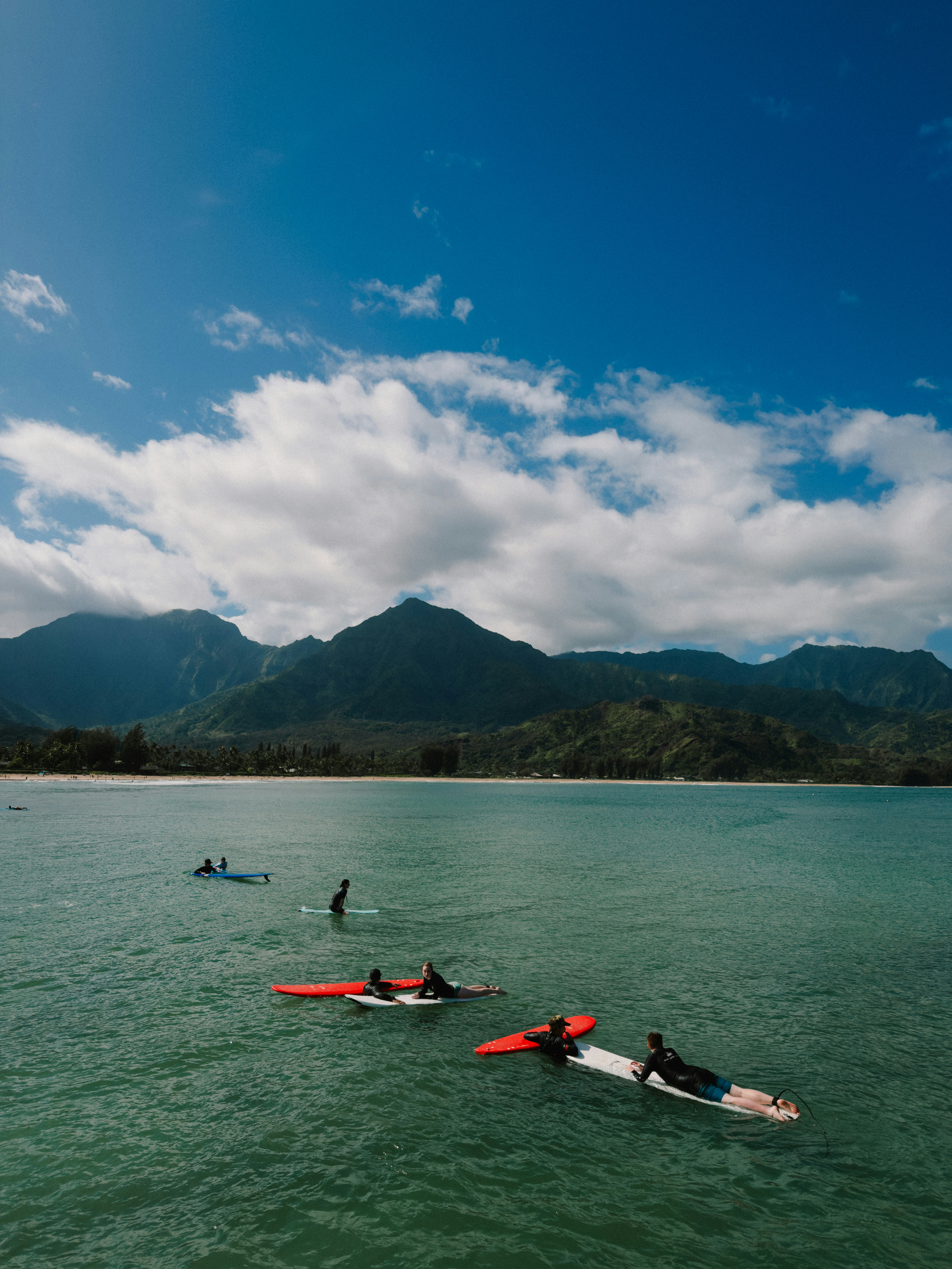 Surfer paddeln auf ruhigem Ozeanwasser mit Bergen dahinter.