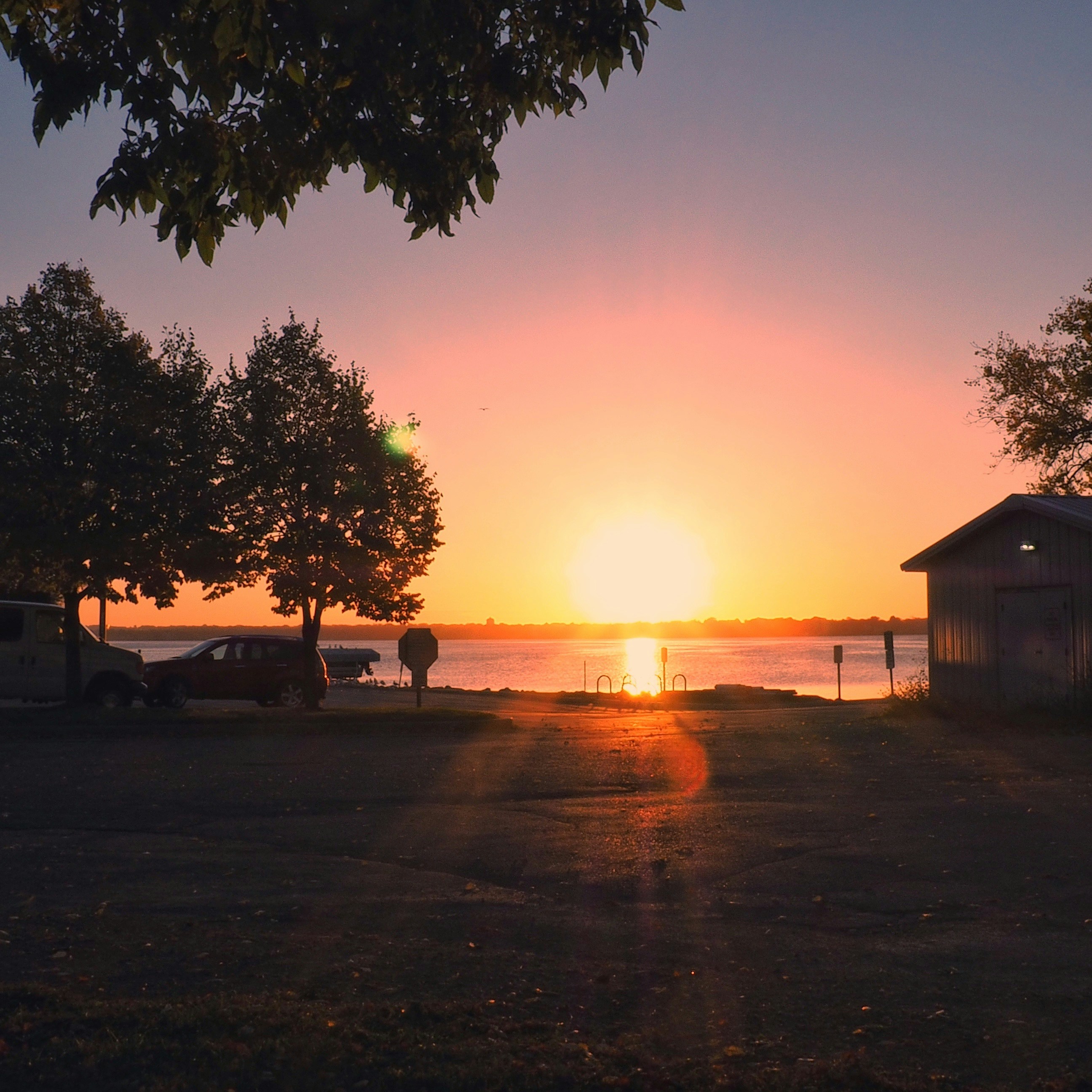 Sunset over a calm lake with trees and a building