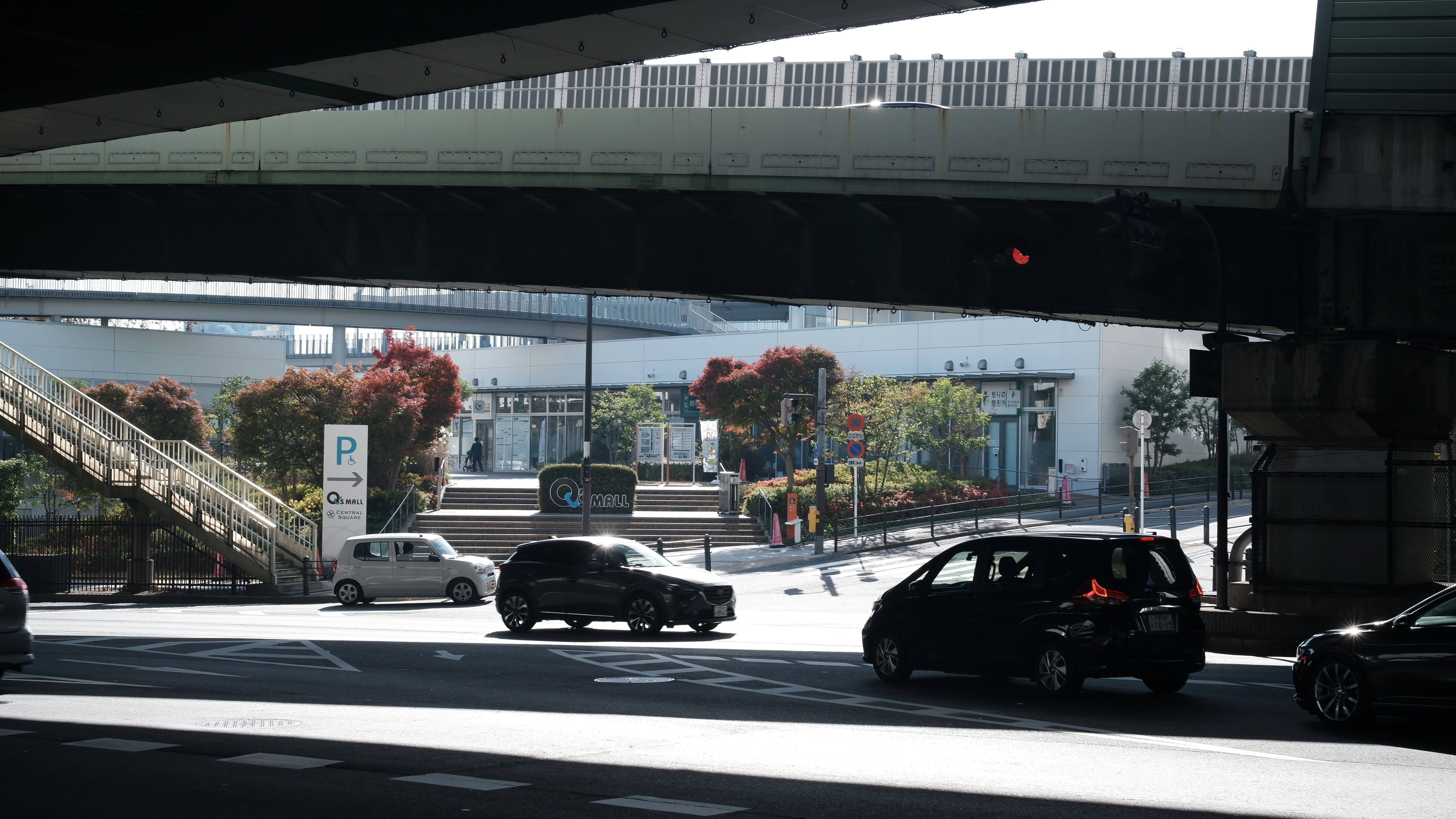 Cars driving under a large overpass on a sunny day.