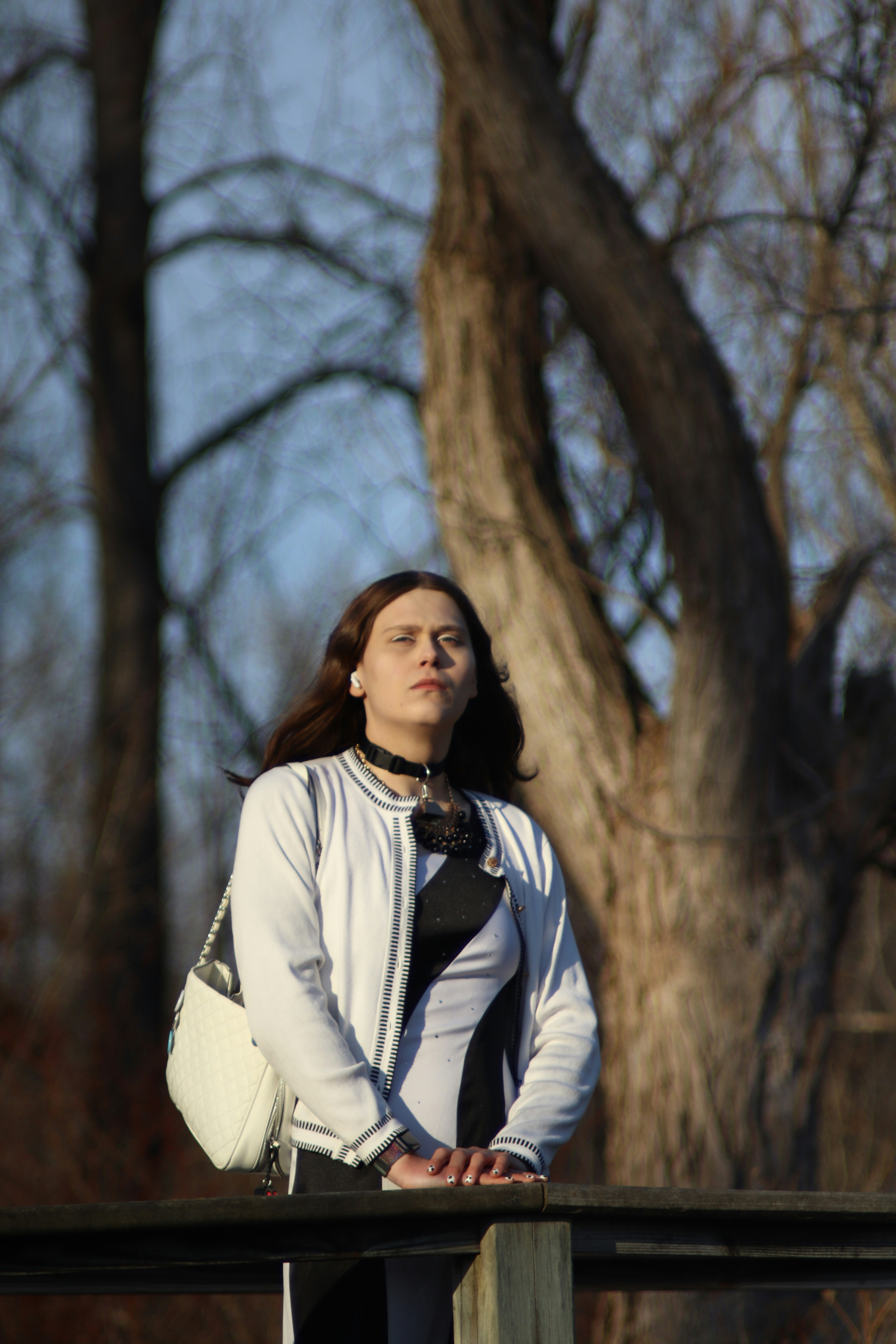 Woman standing outdoors near trees with a handbag