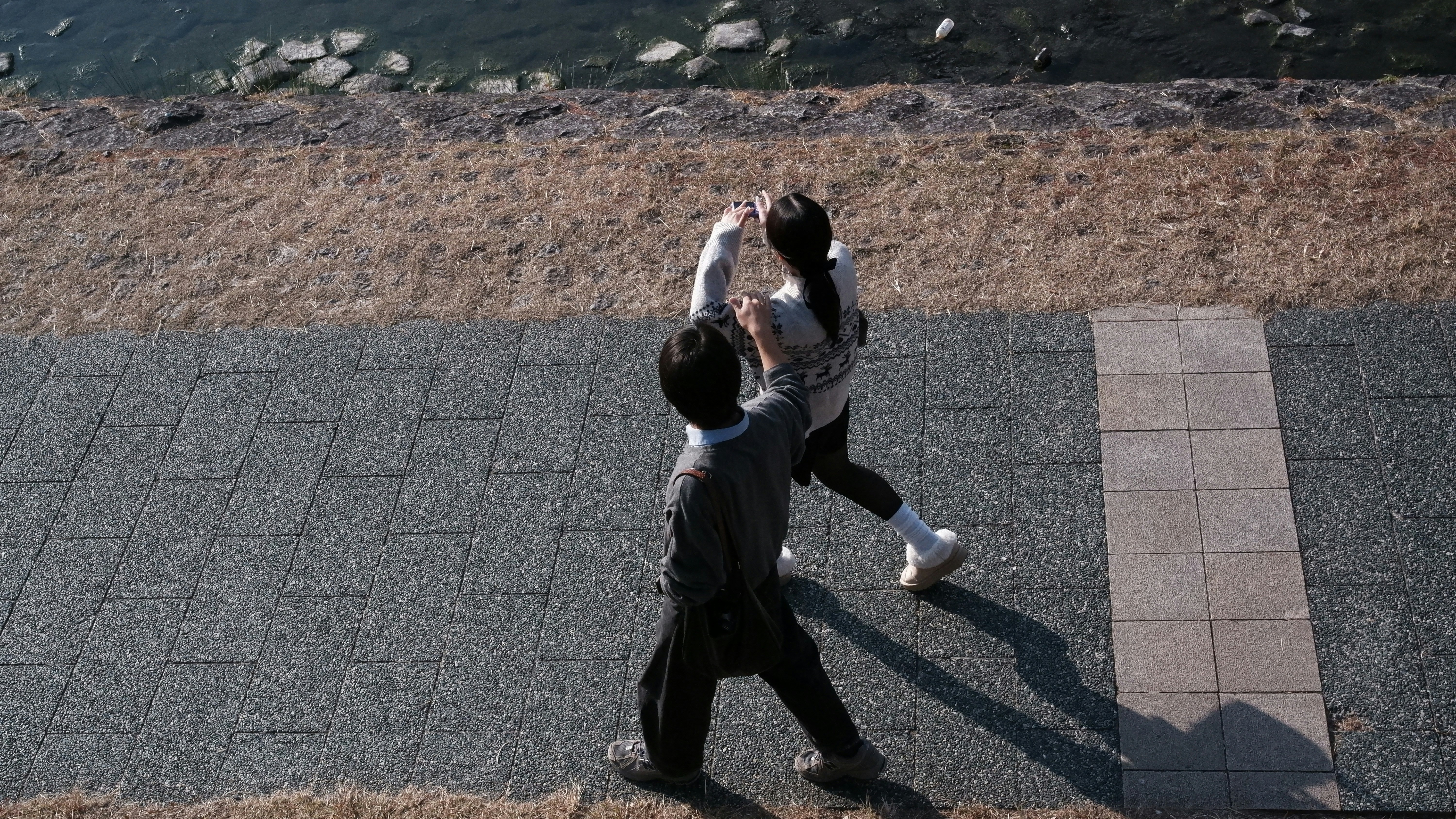 Two people dancing on a paved walkway near water.