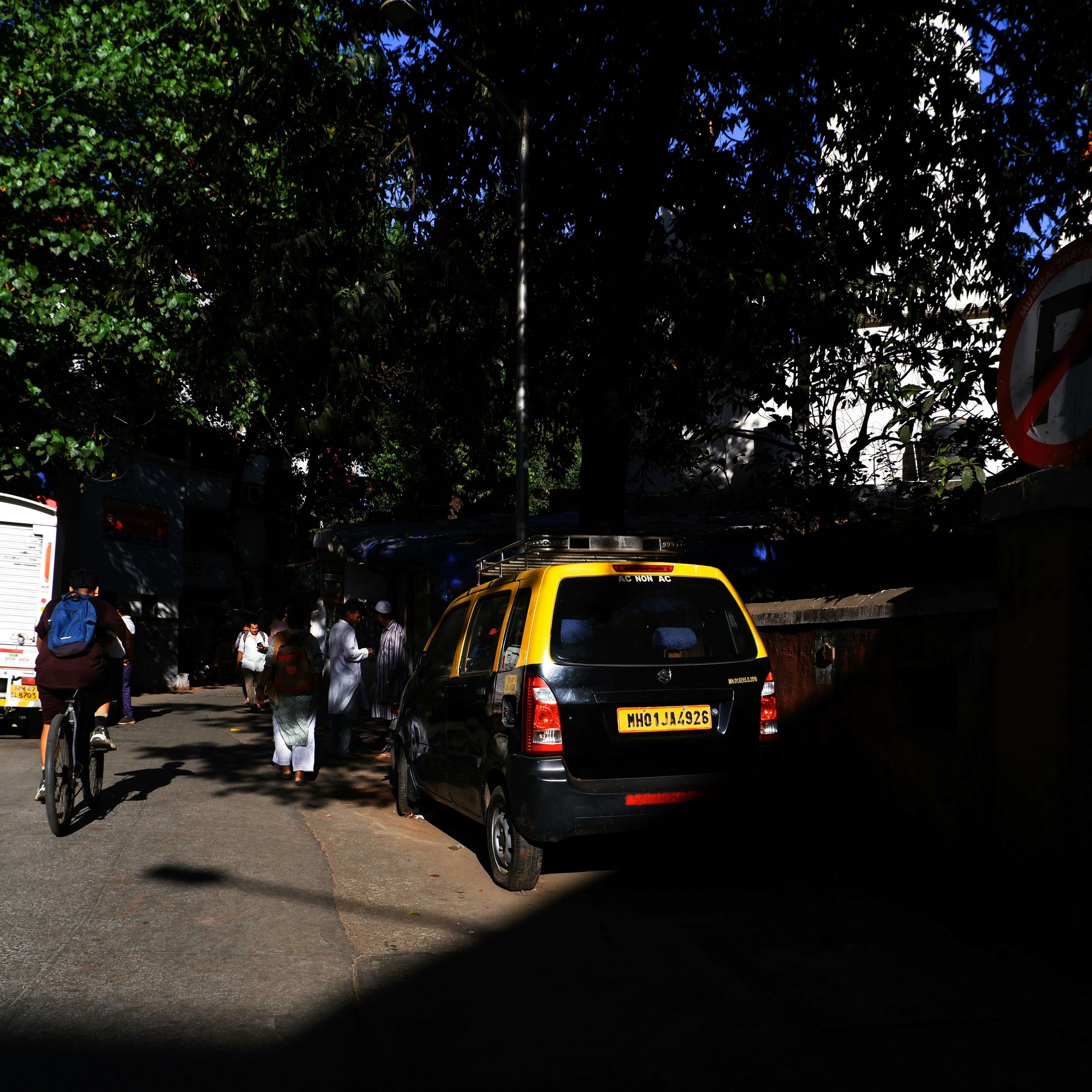 A yellow taxi parked on a street with trees.