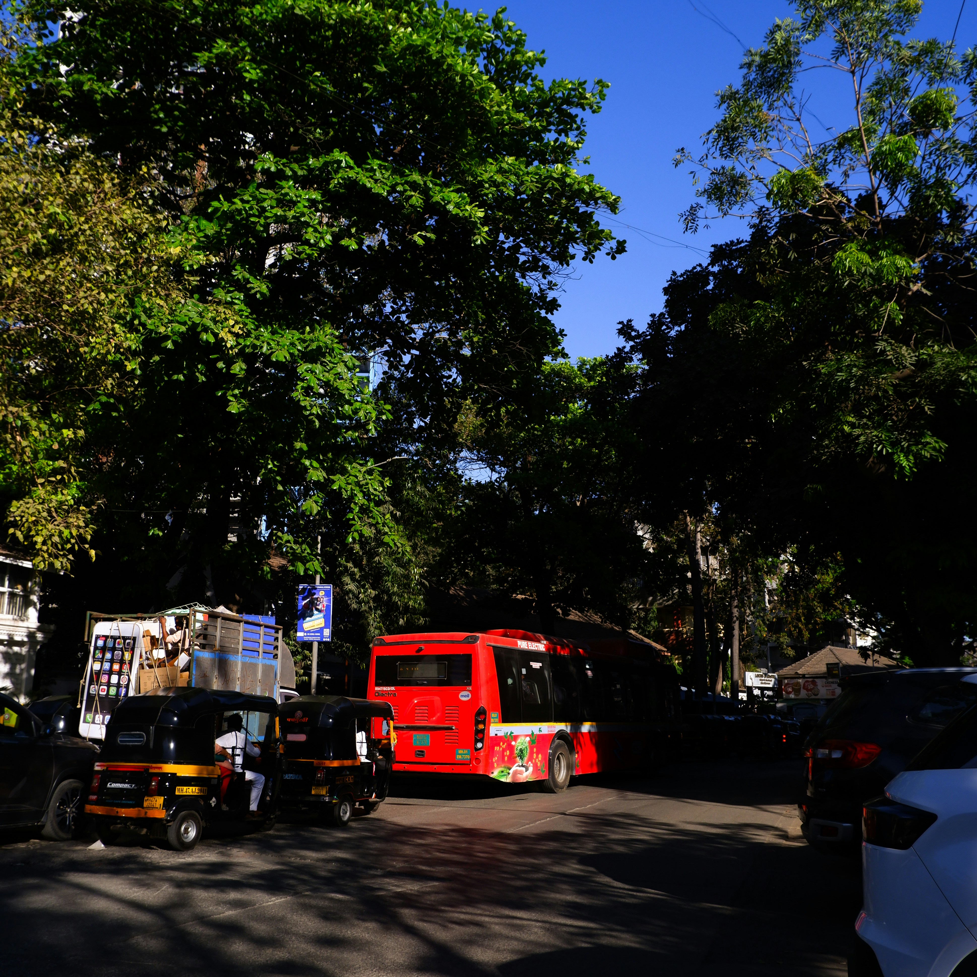 Red bus and auto rickshaws on a street.
