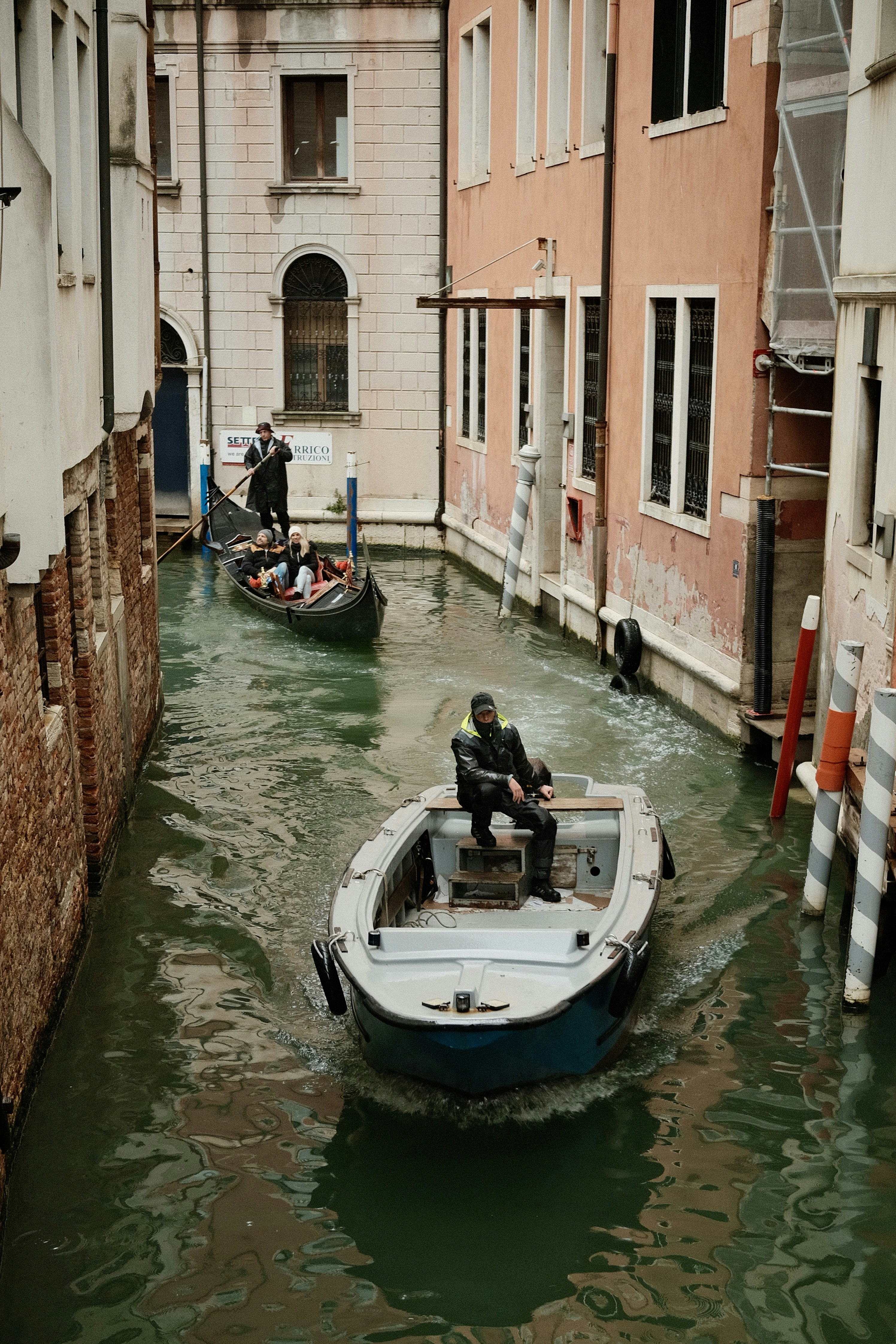Boats navigate a narrow canal between buildings in venice.