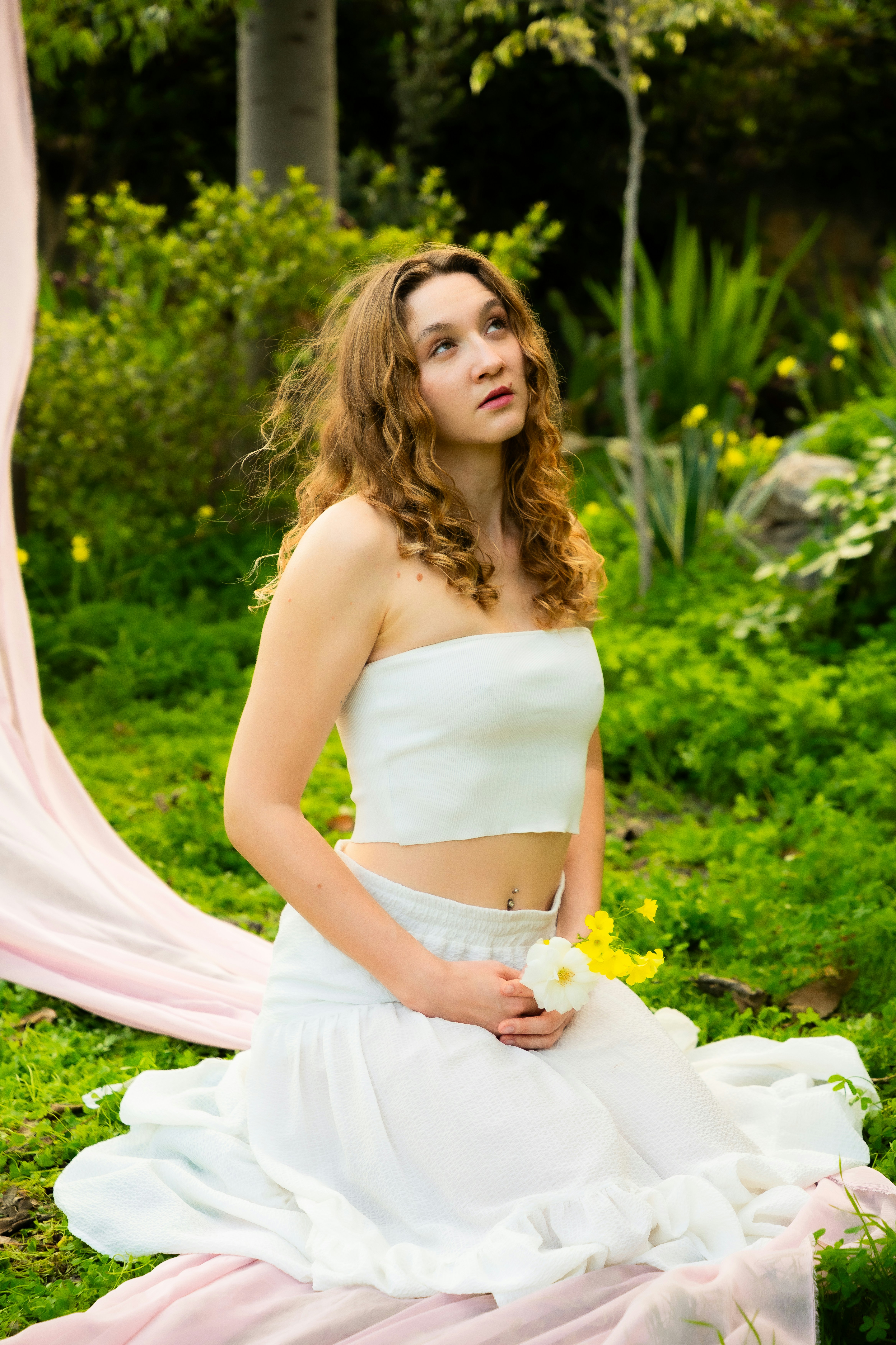 Wanita muda bergaun putih memegang bunga di taman