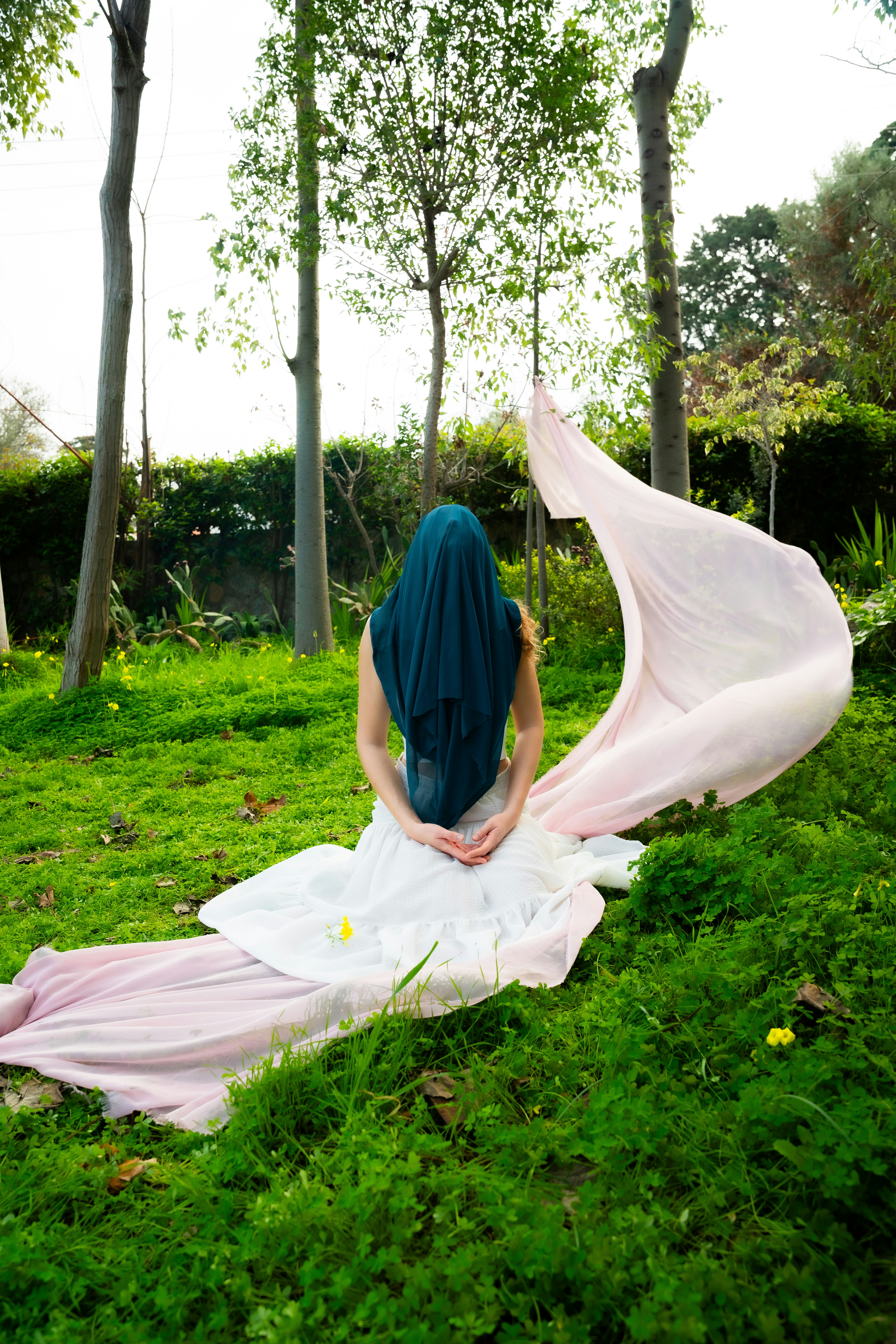 Wanita dengan kain teal menutupi kepala duduk di rumput