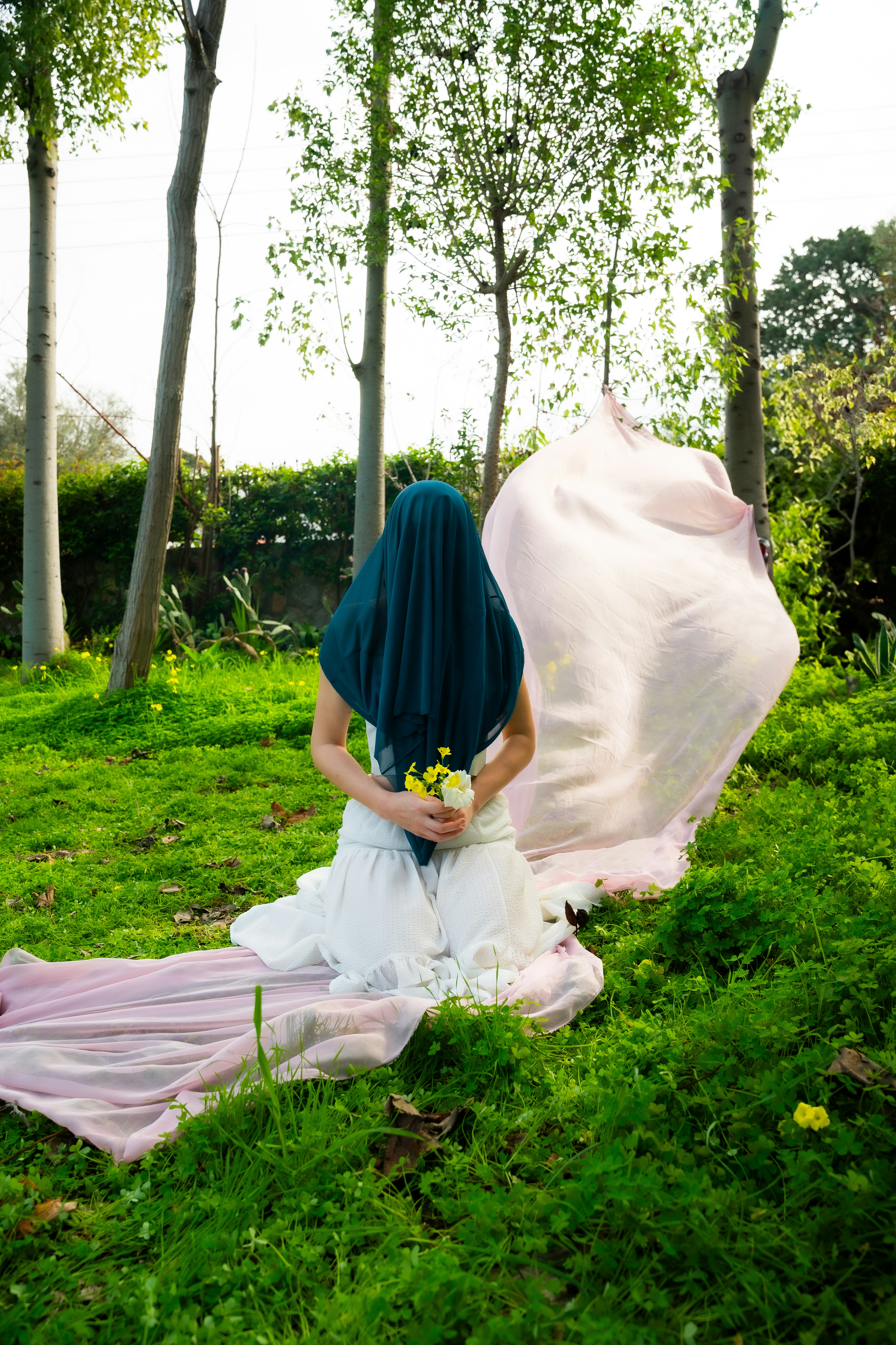 Wanita bergaun putih memegang bunga di taman hijau