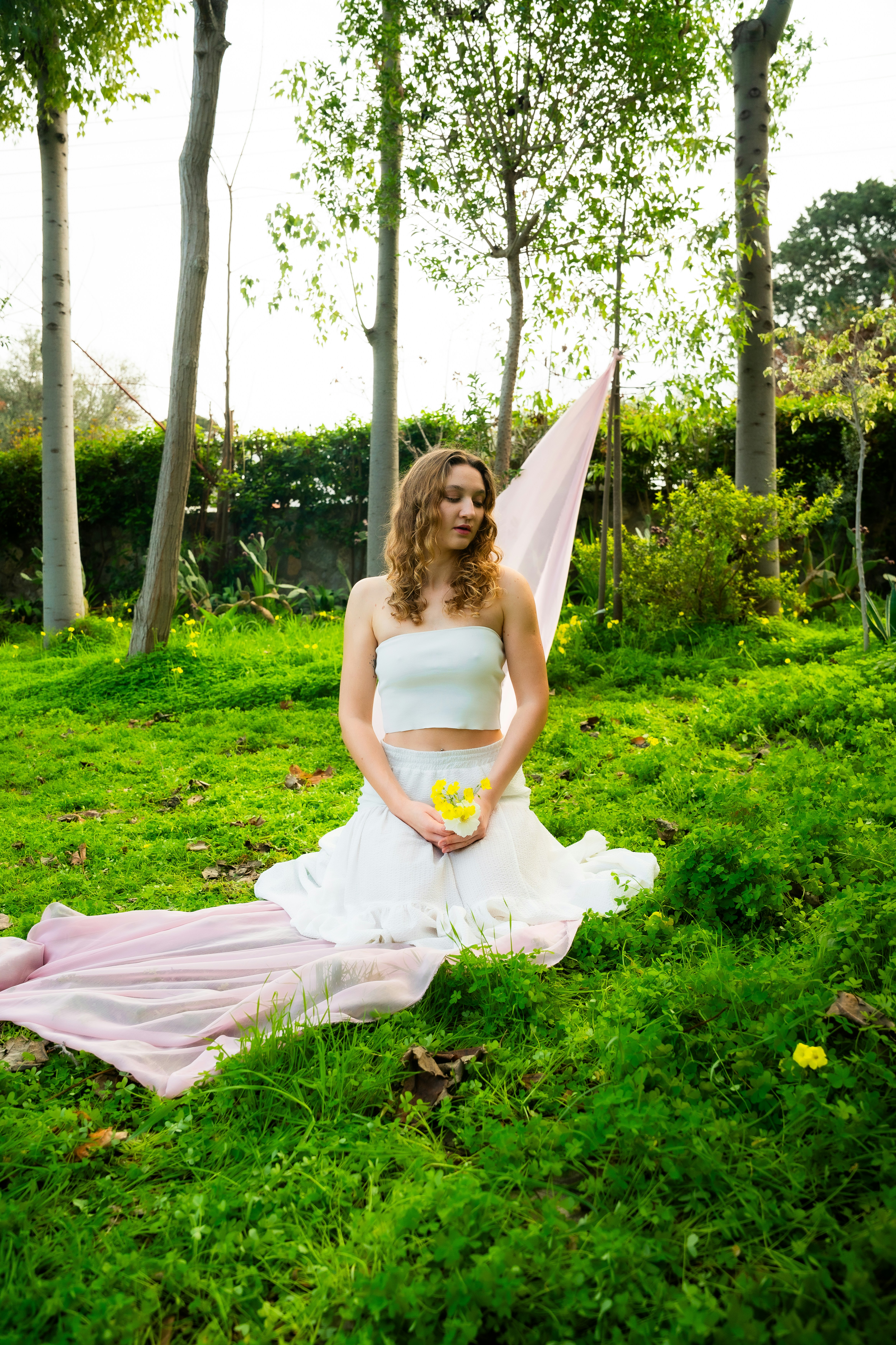 Wanita berpakaian putih memegang bunga kuning di taman