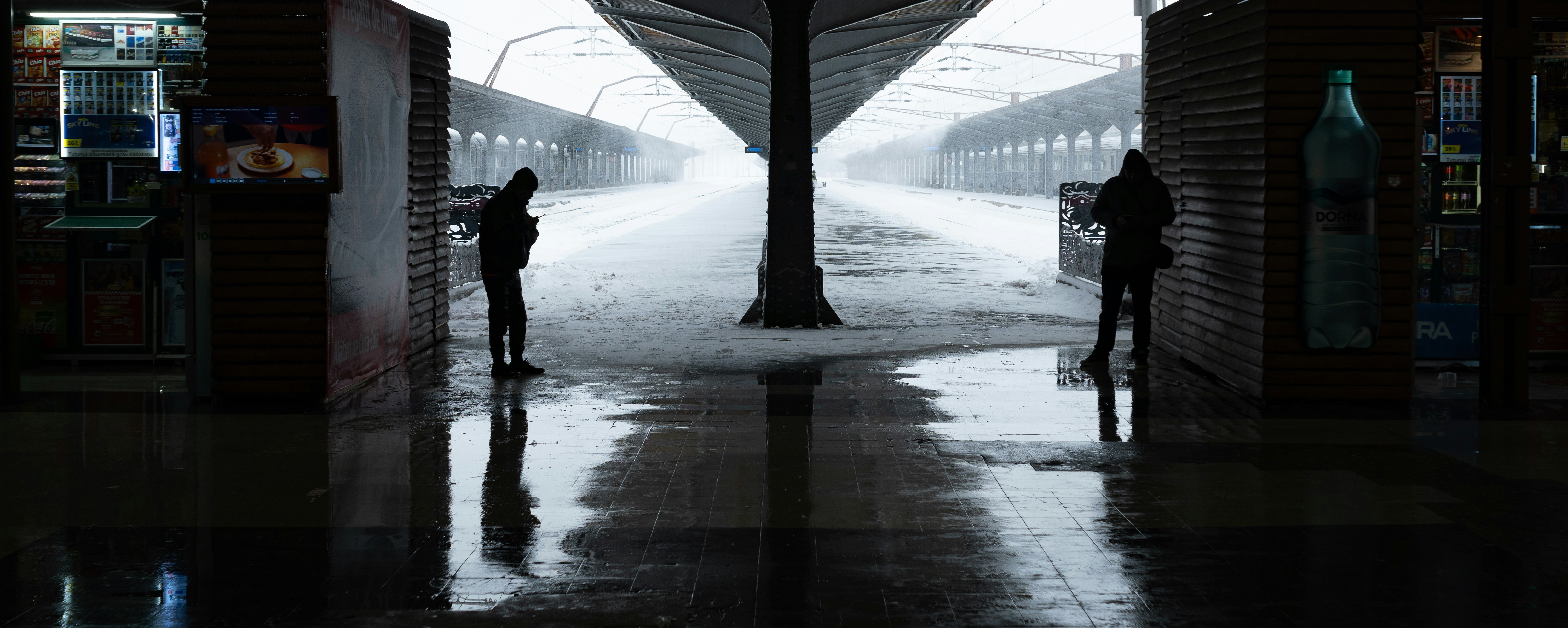 Two people stand on a wet train platform in fog.