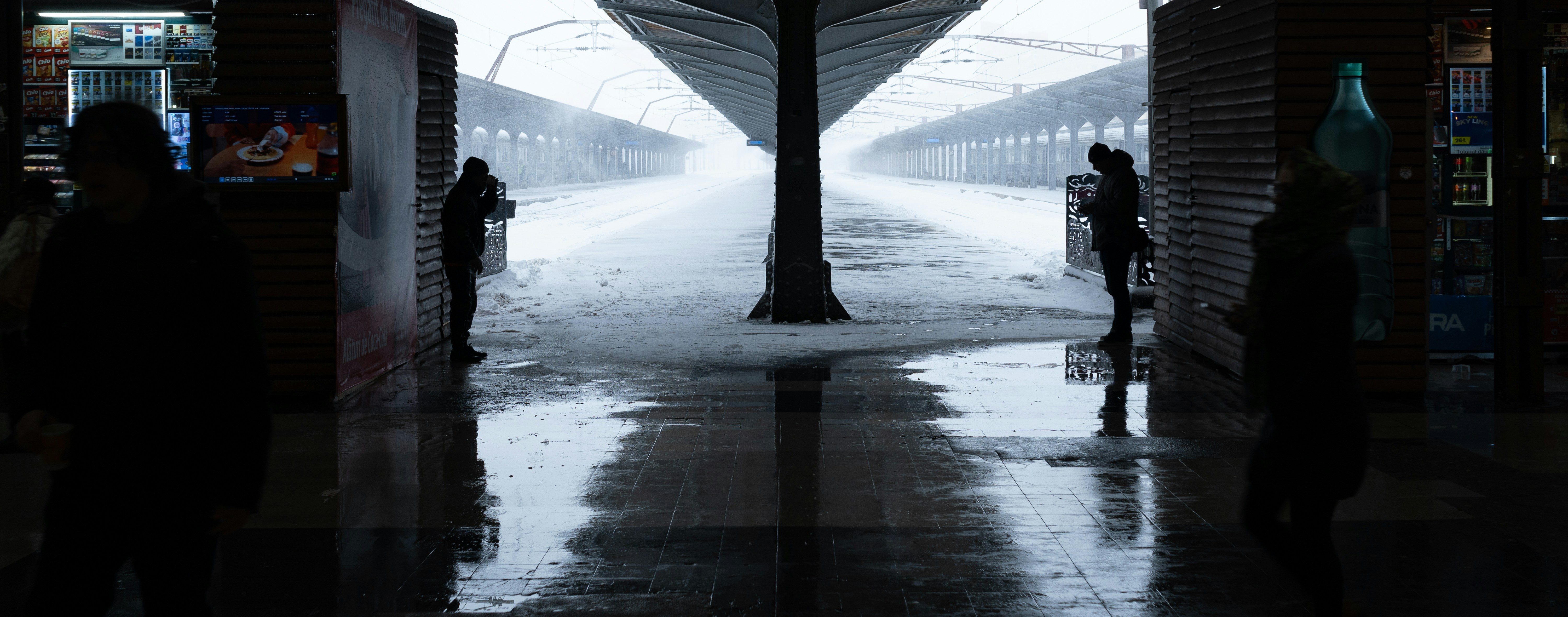 People stand on a wet train platform in the snow.