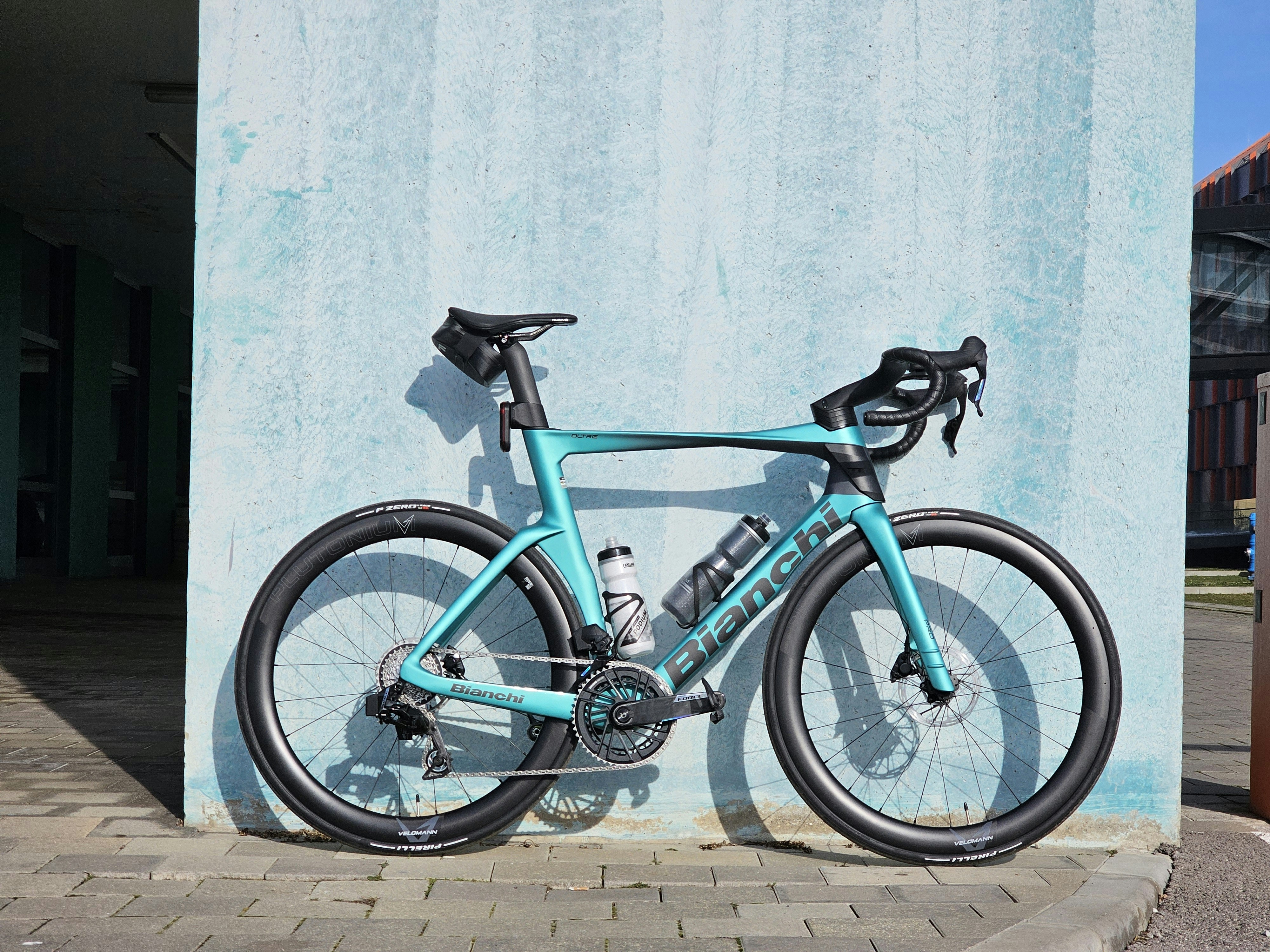 A teal bianchi road bicycle leans against a blue wall.