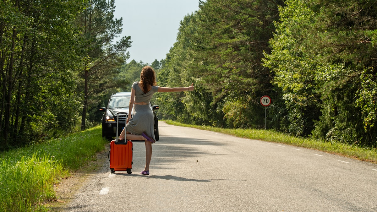Woman hitchhiking with suitcase on roadside