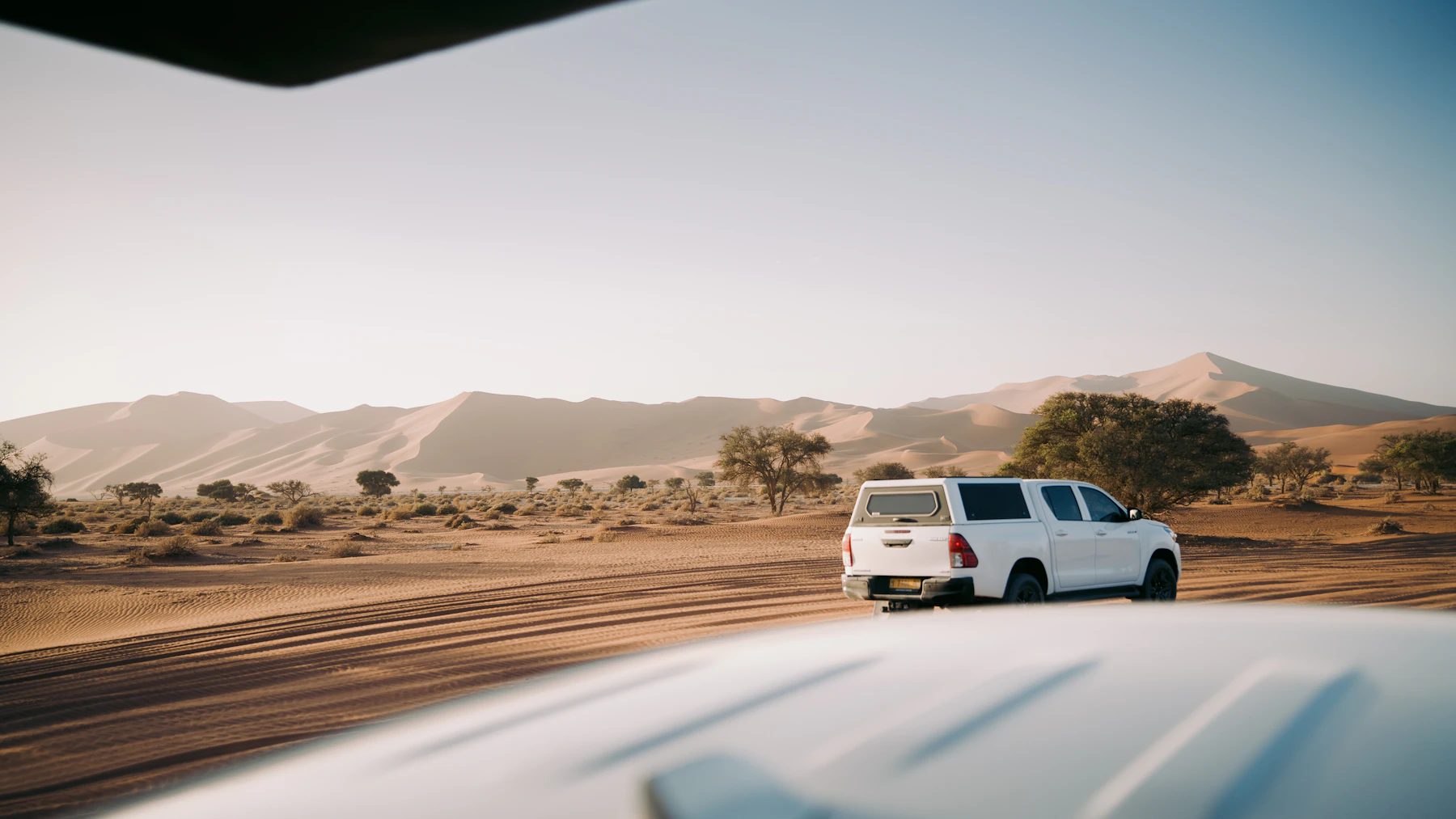 A self-drive four-wheel-drive crosses a sandy track beneath the dunes of Sossusvlei