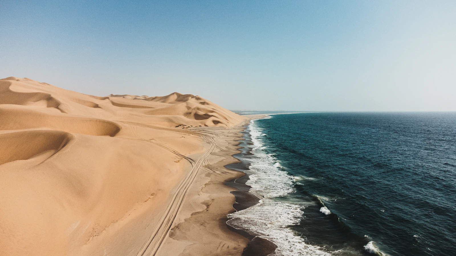 Sandy desert dunes meeting blue ocean waves