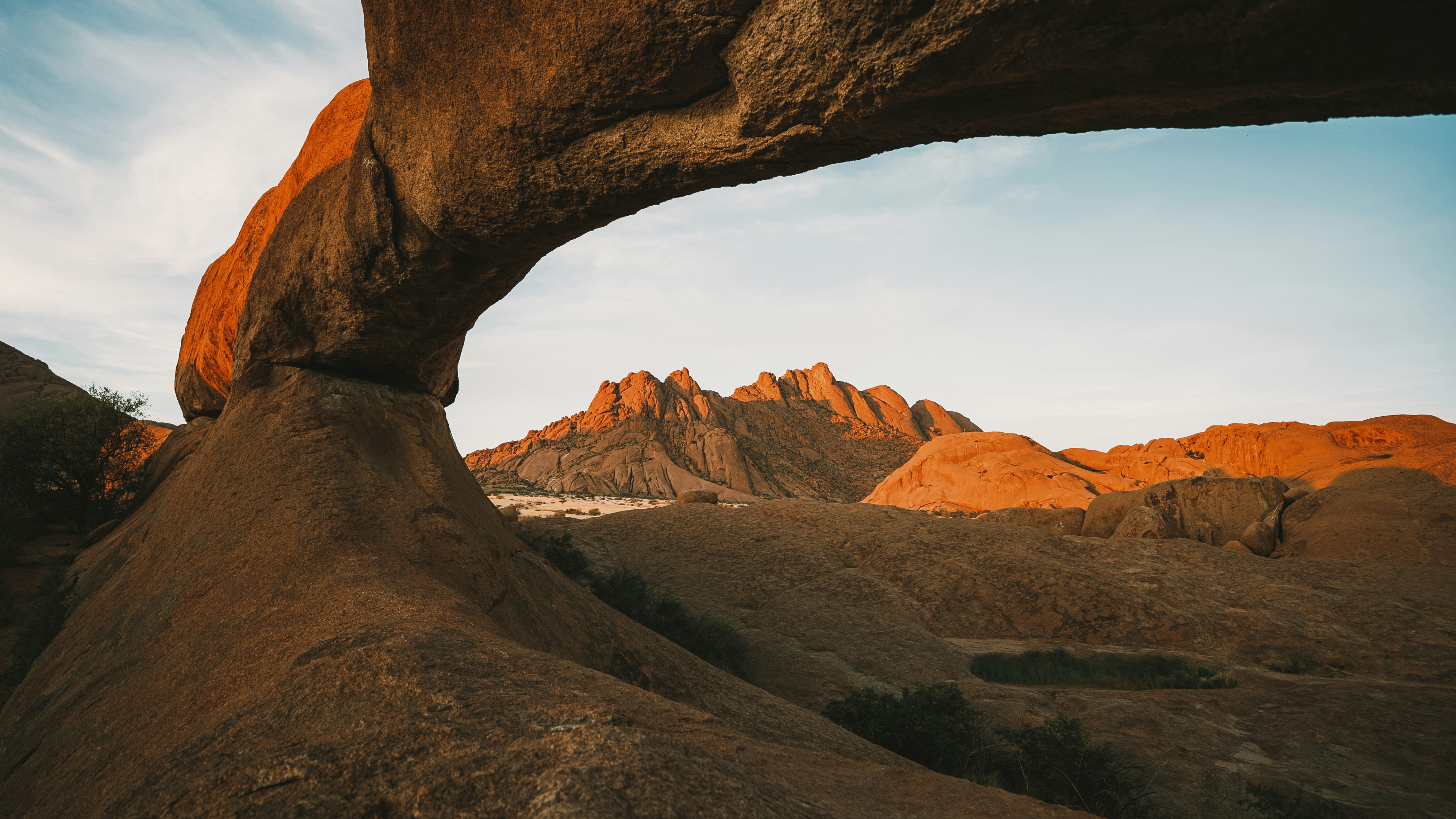 Natural rock arch framing a desert mountain landscape at sunset