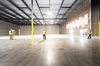 Workers inspect a large, empty industrial warehouse space.