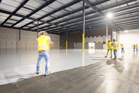 Workers in a large, empty warehouse with polished floors.