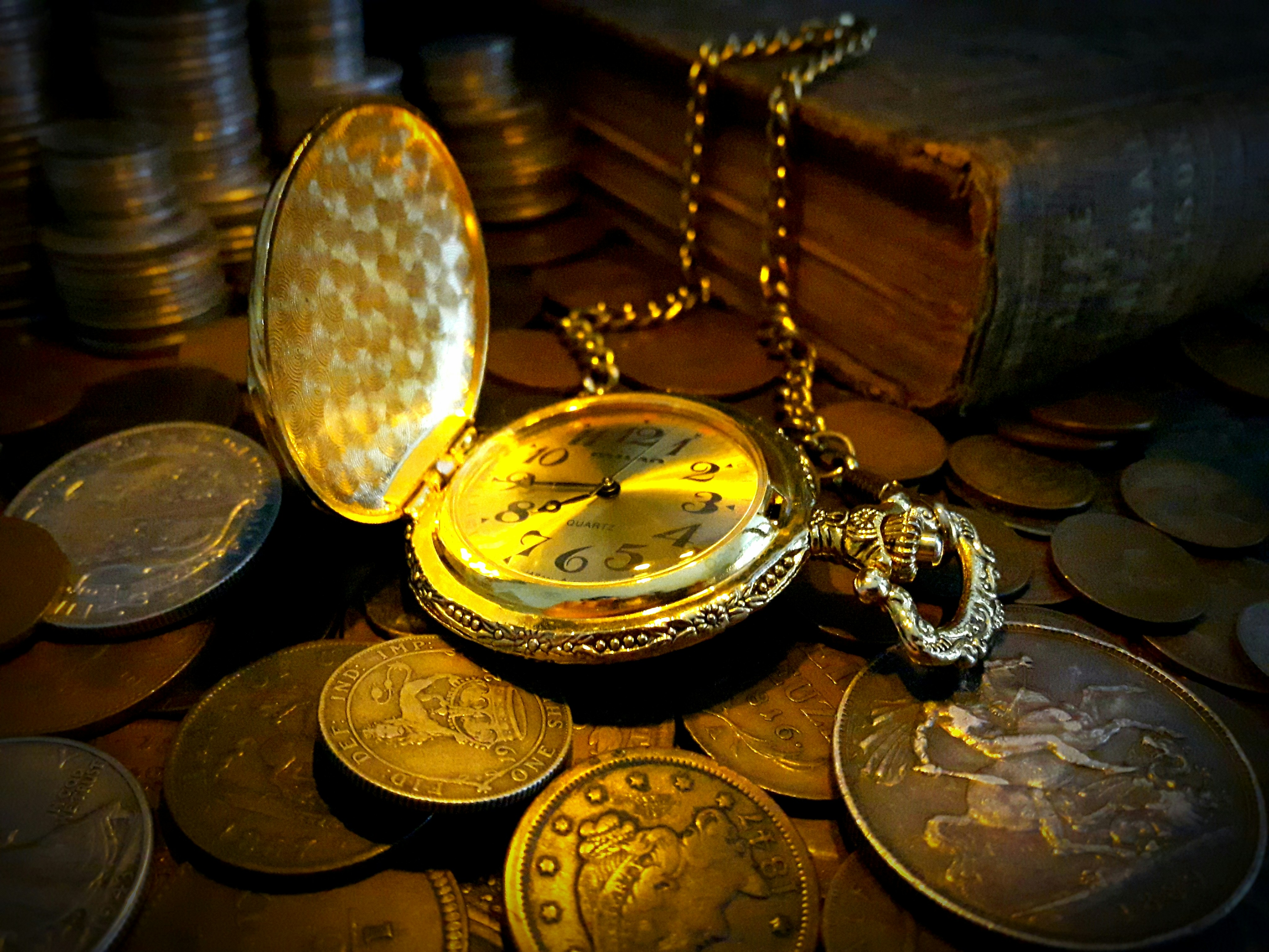 Antique pocket watch surrounded by old coins