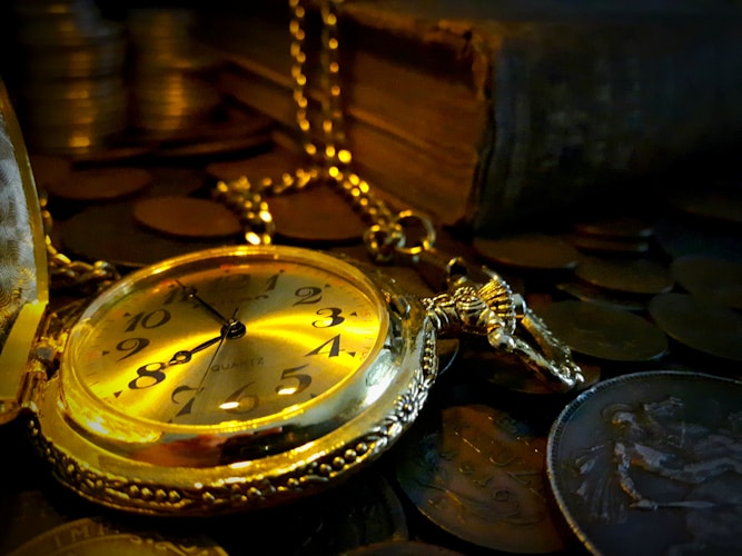 Antique pocket watch resting on old coins and leather-bound books