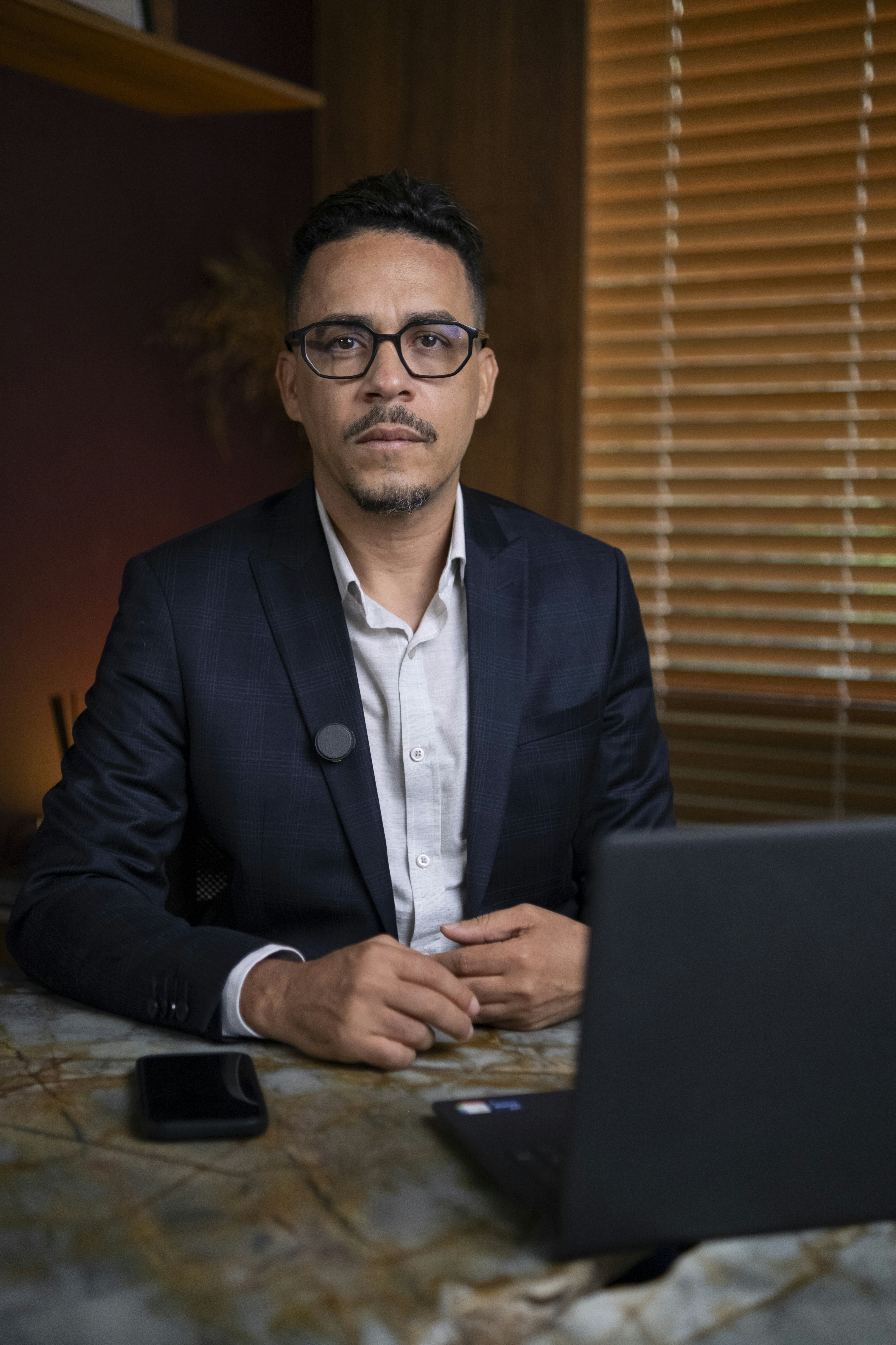 Man in suit sitting at desk with laptop and phone.