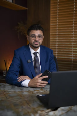 Man in suit holding phone at desk with laptop