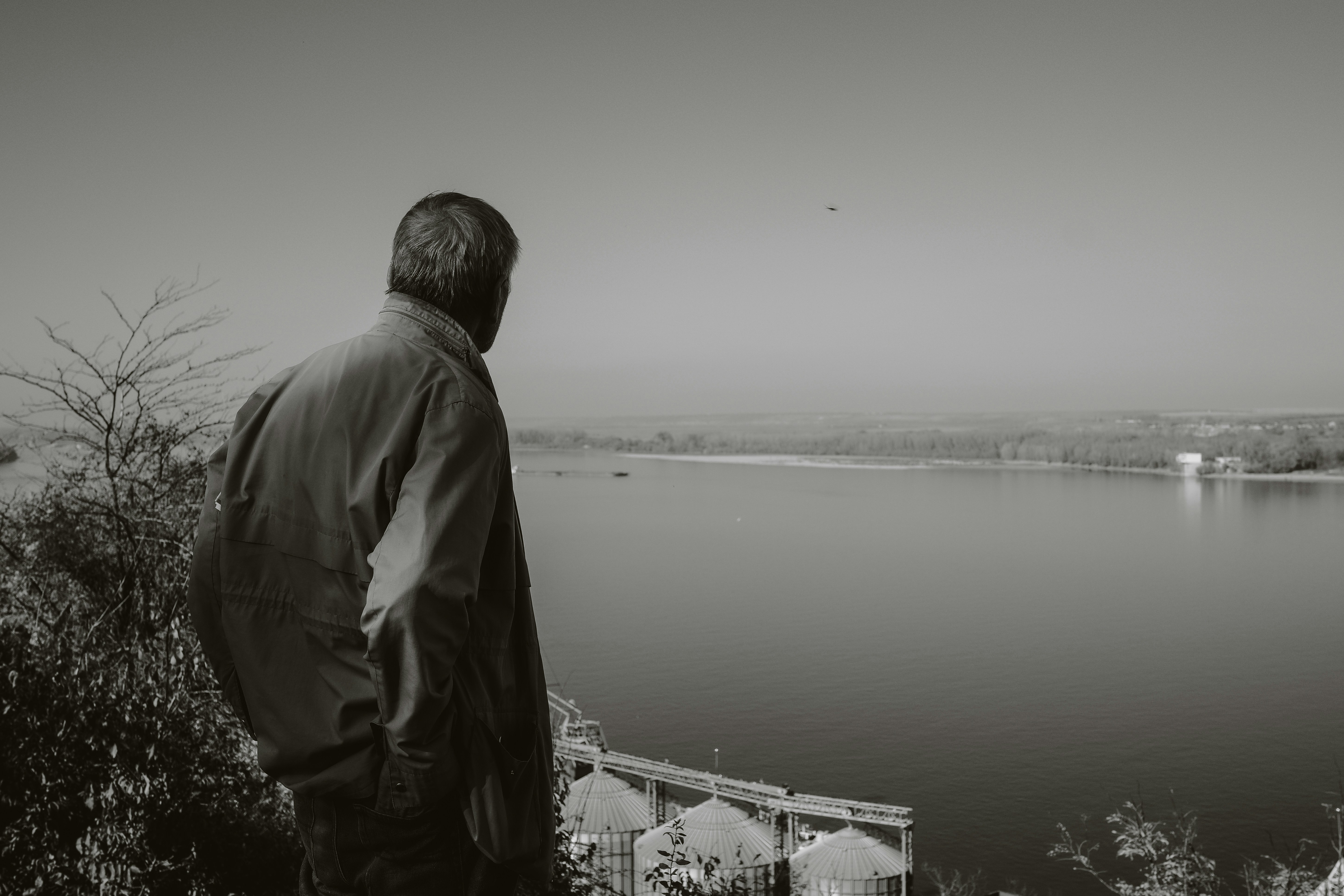 A grayscale photo of an elderly man with deep lines on his face, looking sadly into the distance, perhaps in a rural setting.