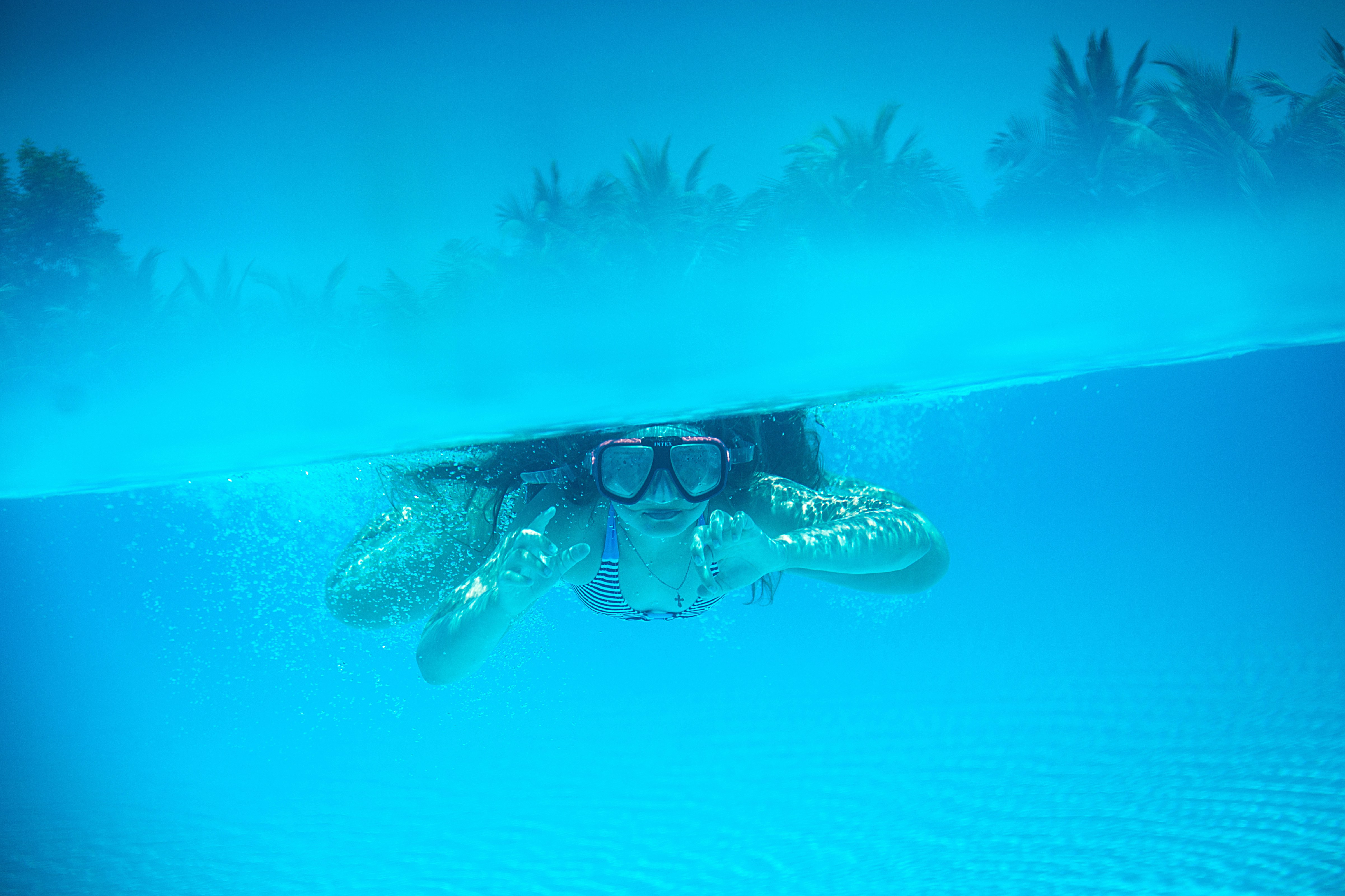 A person wearing a mask swims underwater in a pool.