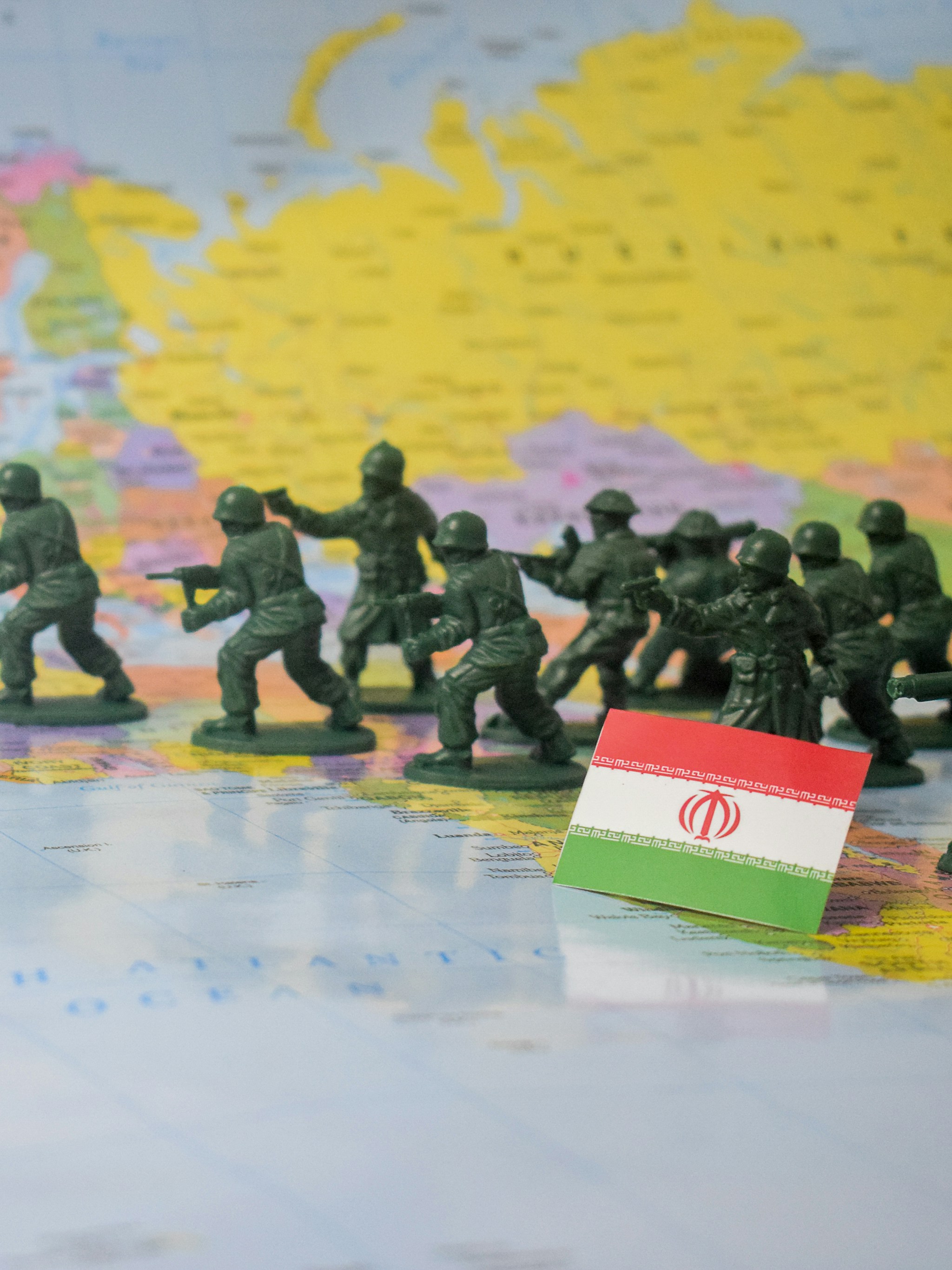 Toy soldiers advance across a world map near iran's flag.