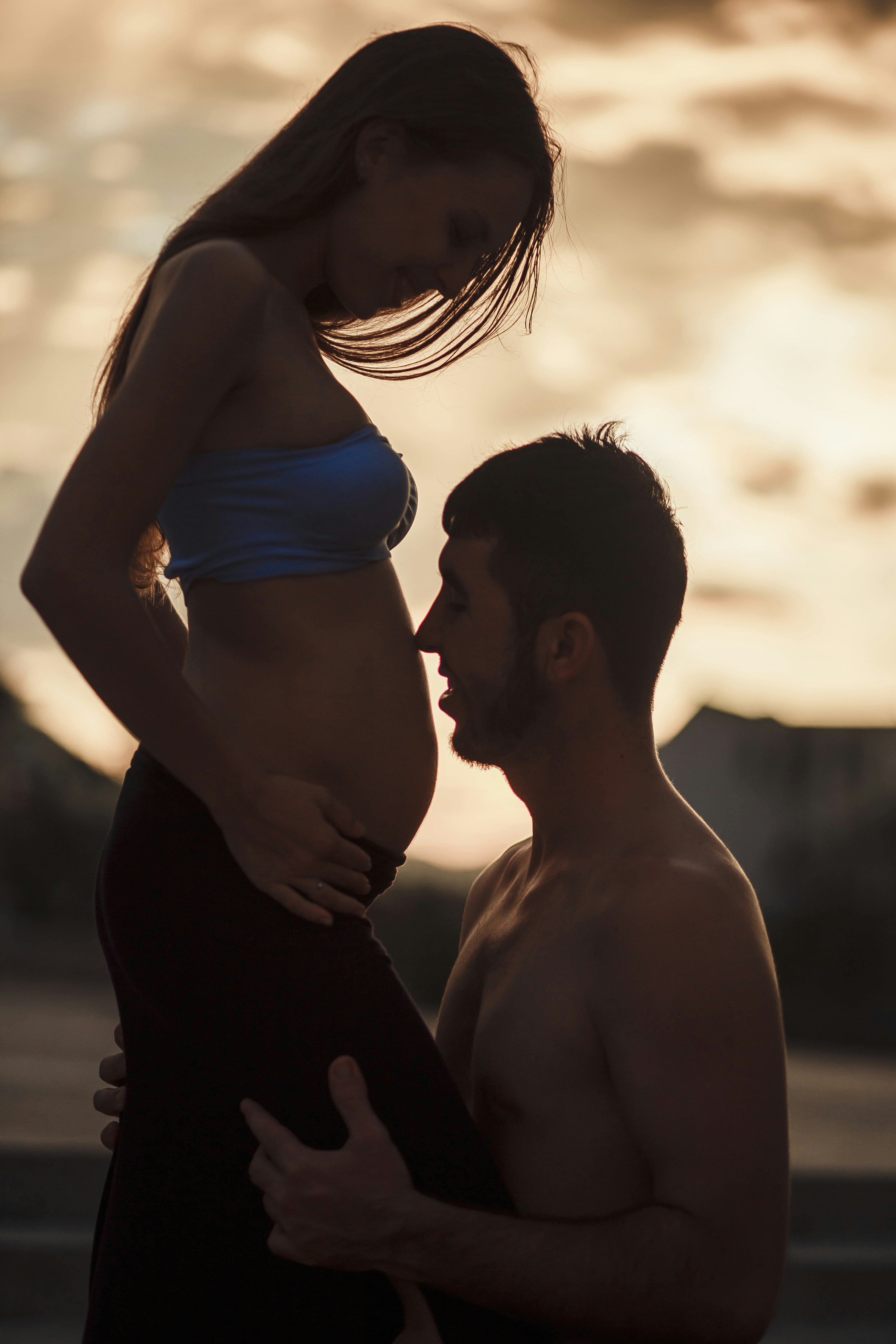 Paar umarmt sich bei Sonnenuntergang mit schwangerem Bauch.