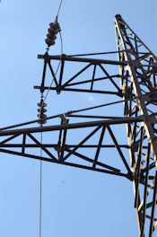 Close-up of a metal power line tower against blue sky