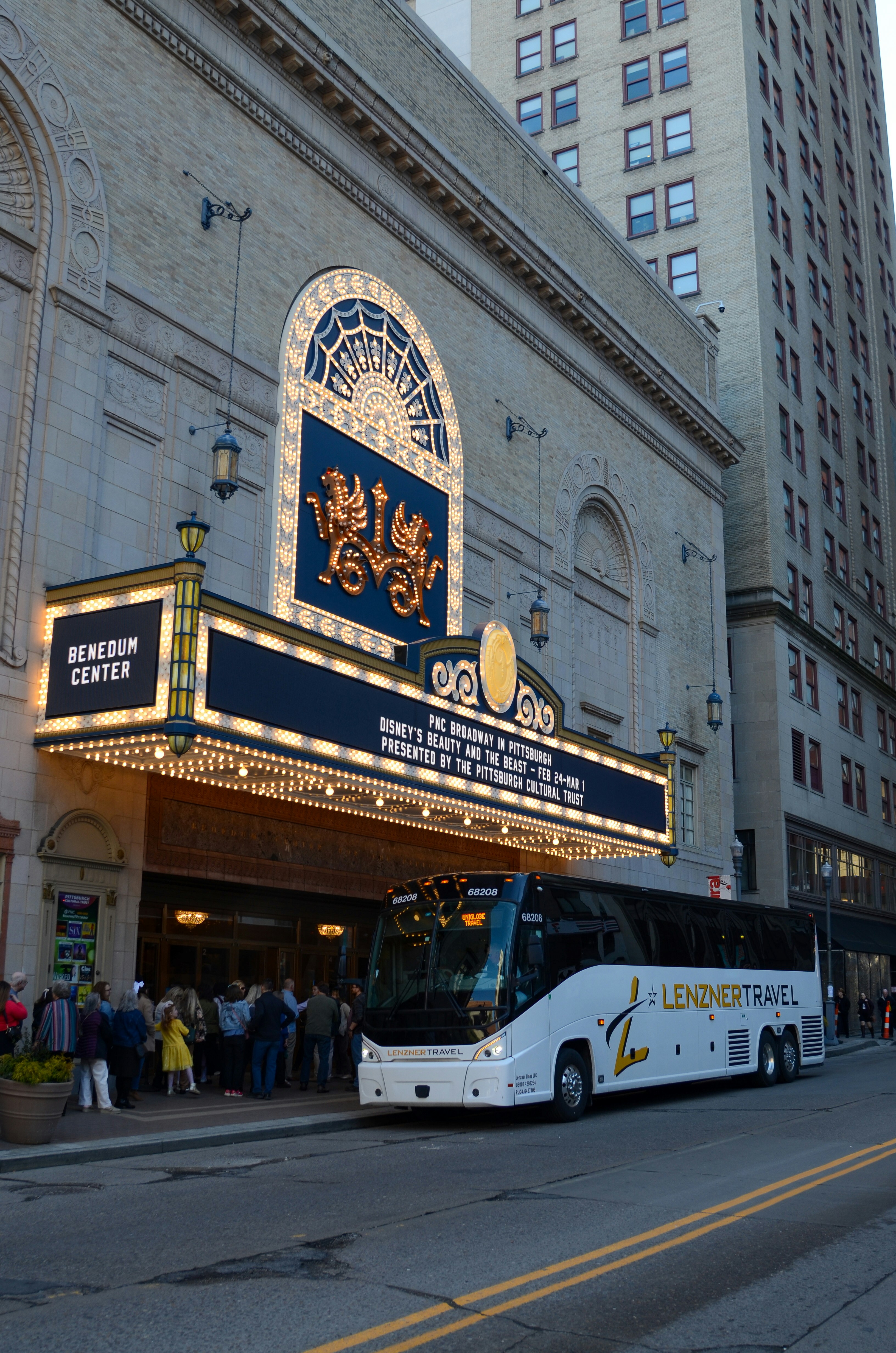 A tour bus parked outside a theater entrance.