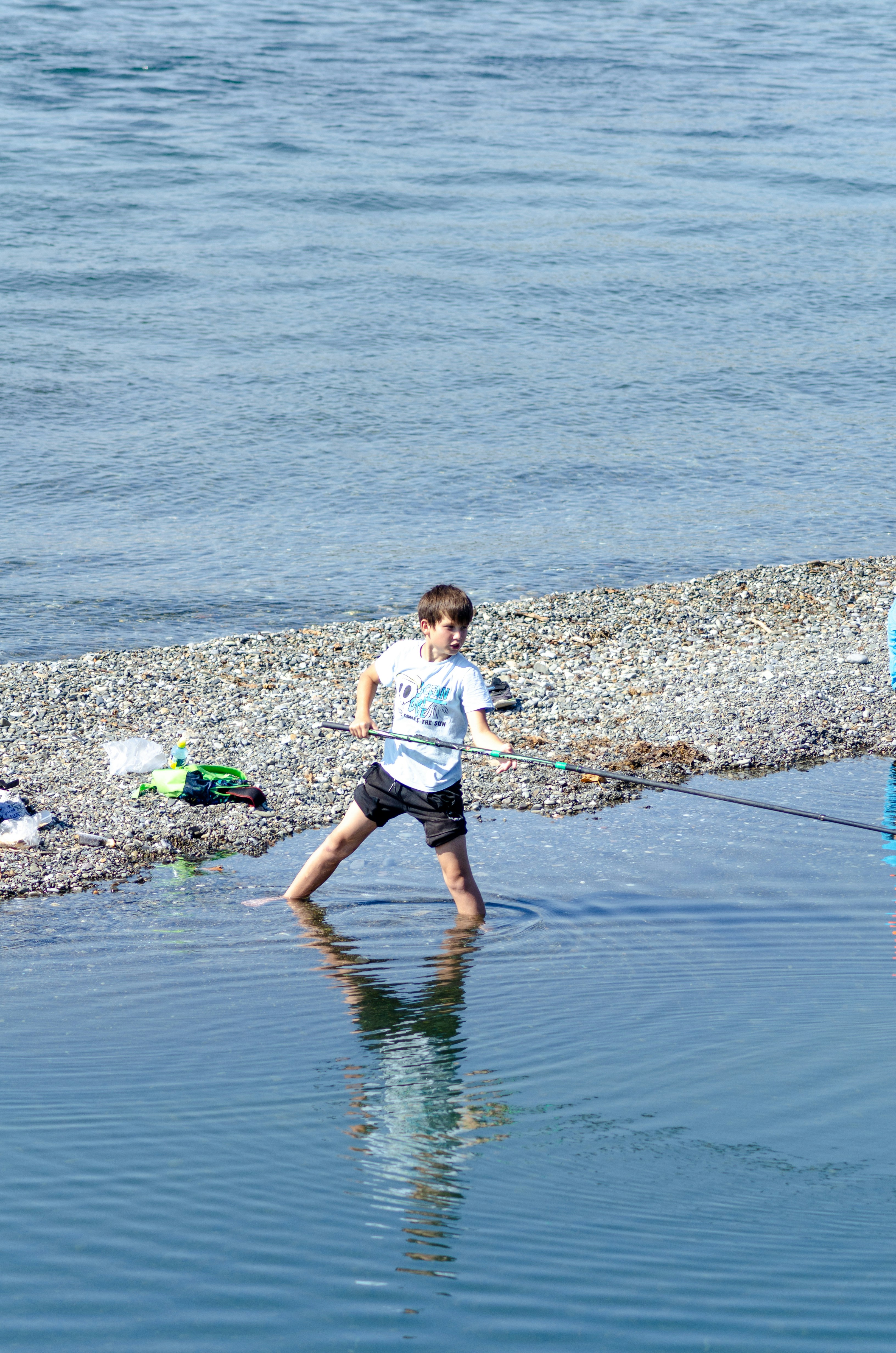 Junge, der in flachem Wasser in der Nähe eines Kiesstrandes watet